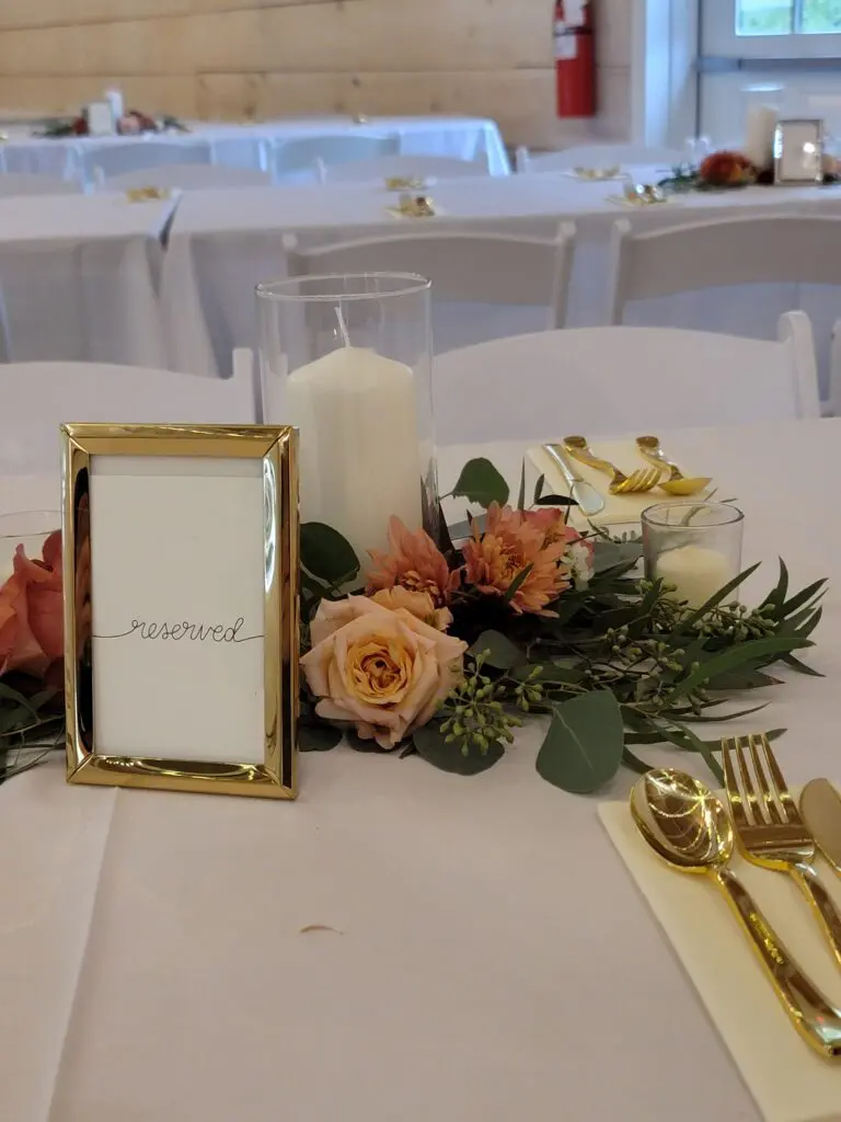 A table with flowers , candles , and a picture frame on it.