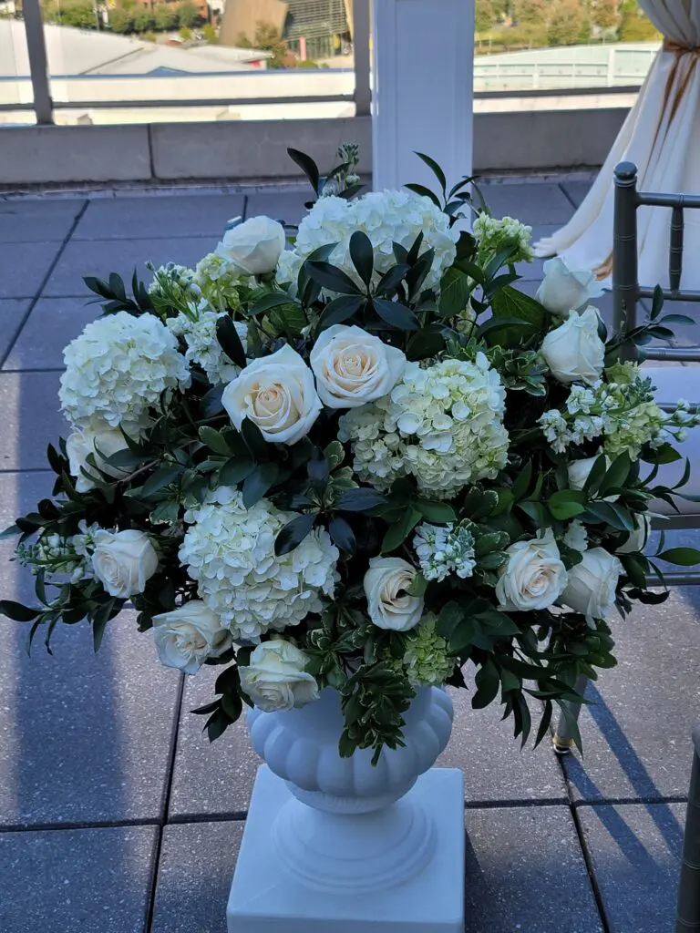 A vase filled with white flowers and greenery is sitting on a tiled floor.
