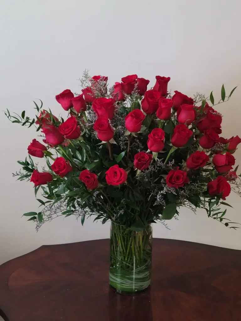 A vase filled with red roses is sitting on a wooden table.