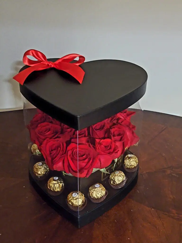 A heart shaped box filled with red roses and chocolates.