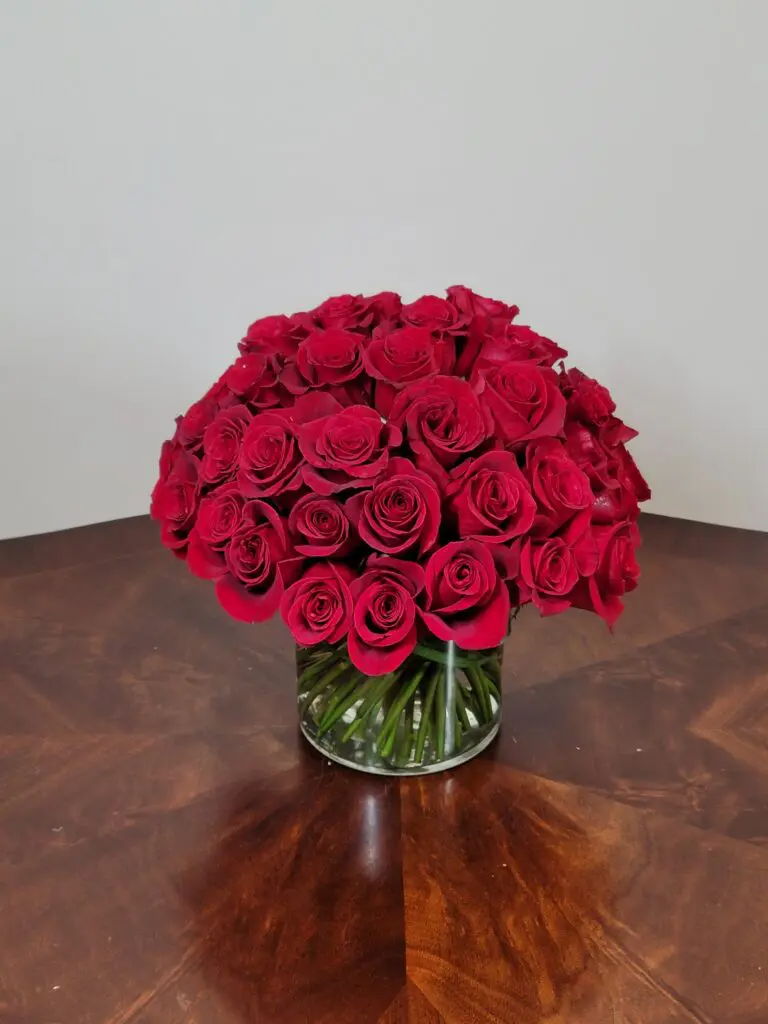 A vase filled with red roses is sitting on a wooden table.