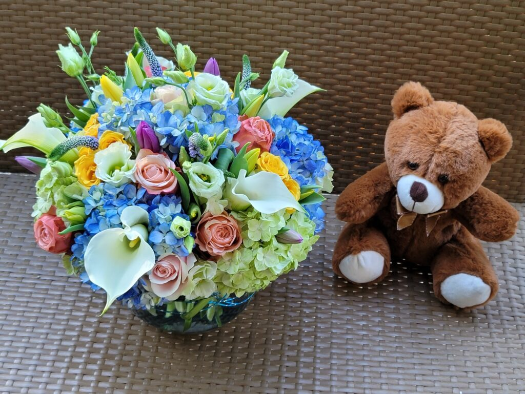 A teddy bear is sitting next to a vase of flowers