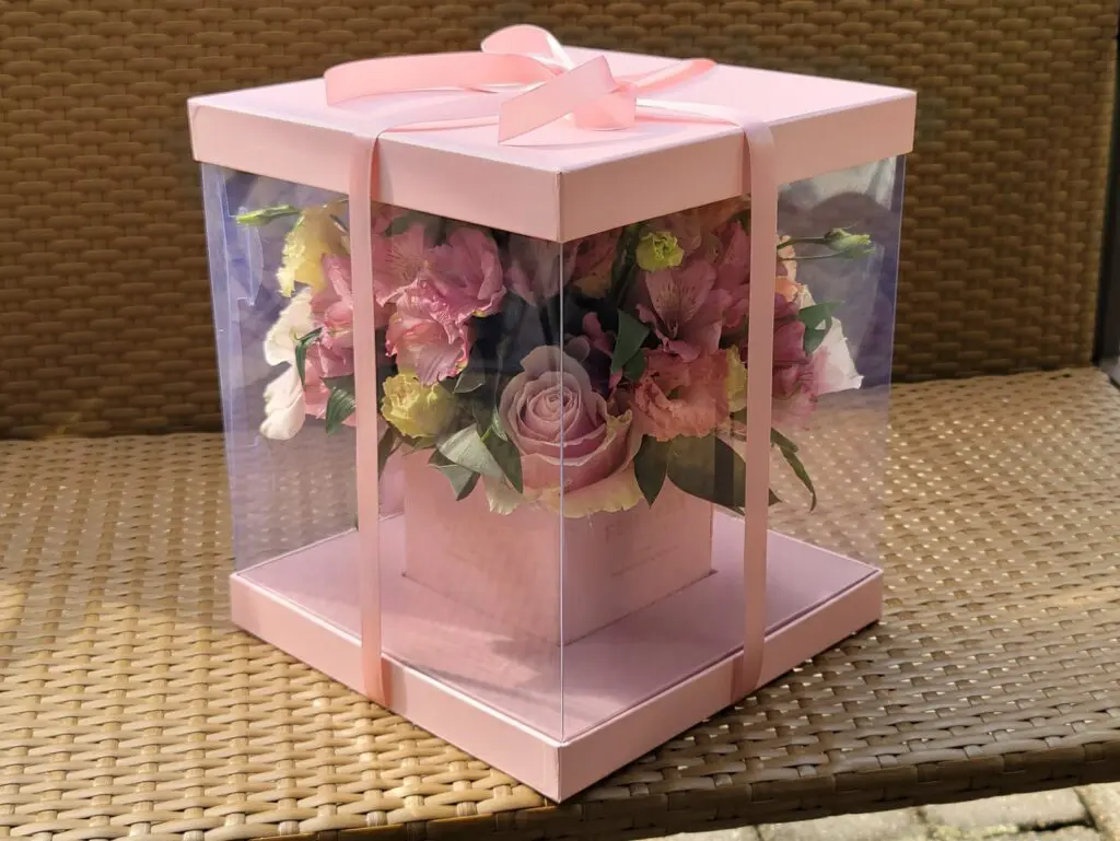 A pink box filled with flowers is sitting on a wicker table.