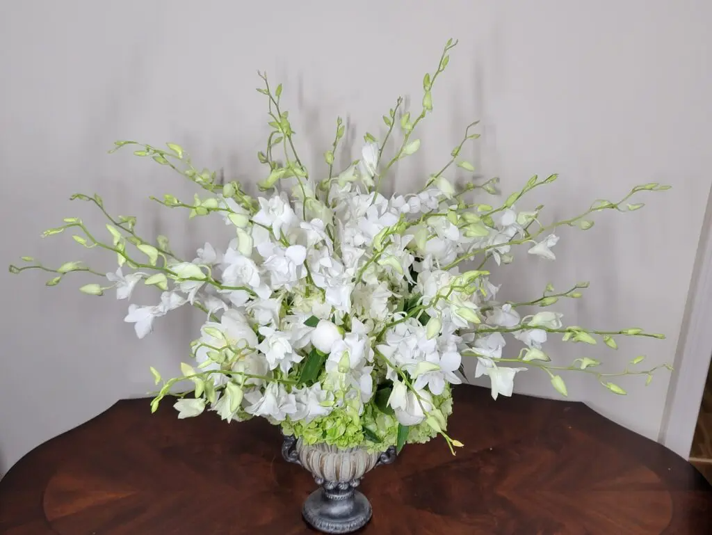 A vase filled with white flowers is sitting on a wooden table.