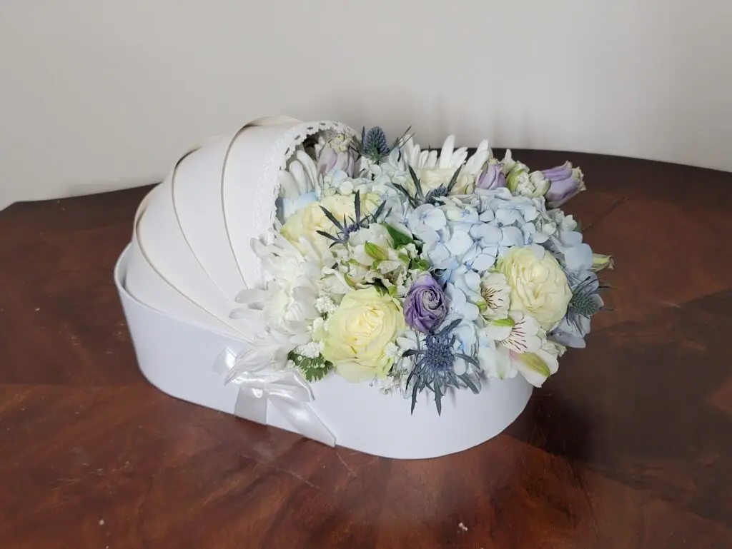 A white cradle filled with flowers on a wooden table