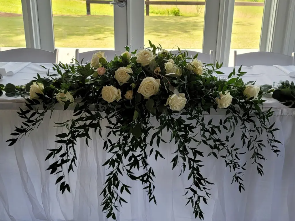A long white table with flowers and greenery on it.