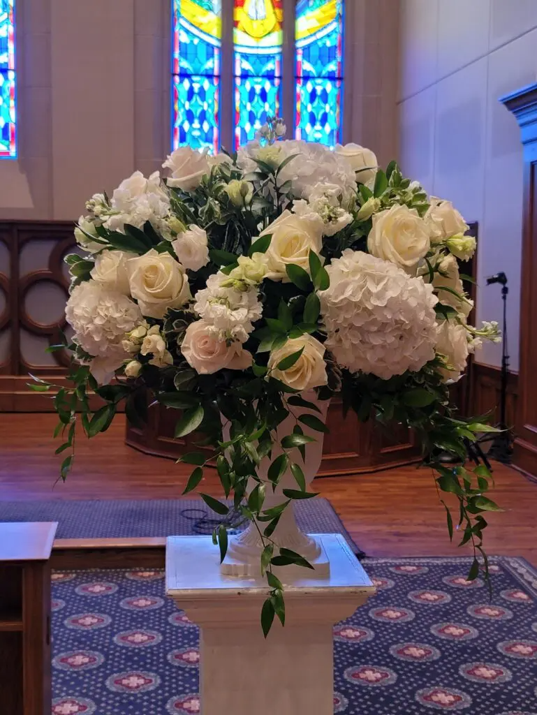 A vase filled with white flowers is sitting on a pedestal in a church.