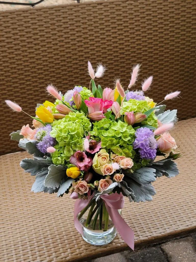 A vase filled with flowers is sitting on a wicker bench.