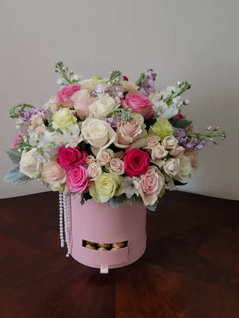 A pink box filled with flowers is sitting on a wooden table.
