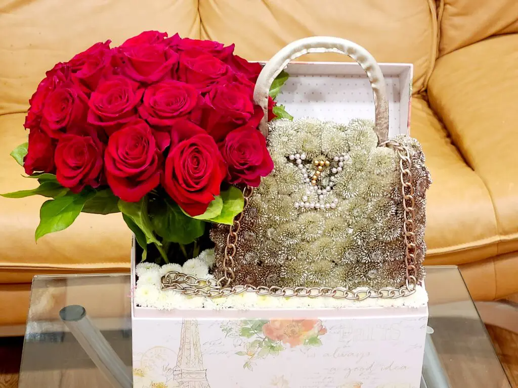 A box filled with red roses and a purse on a table.