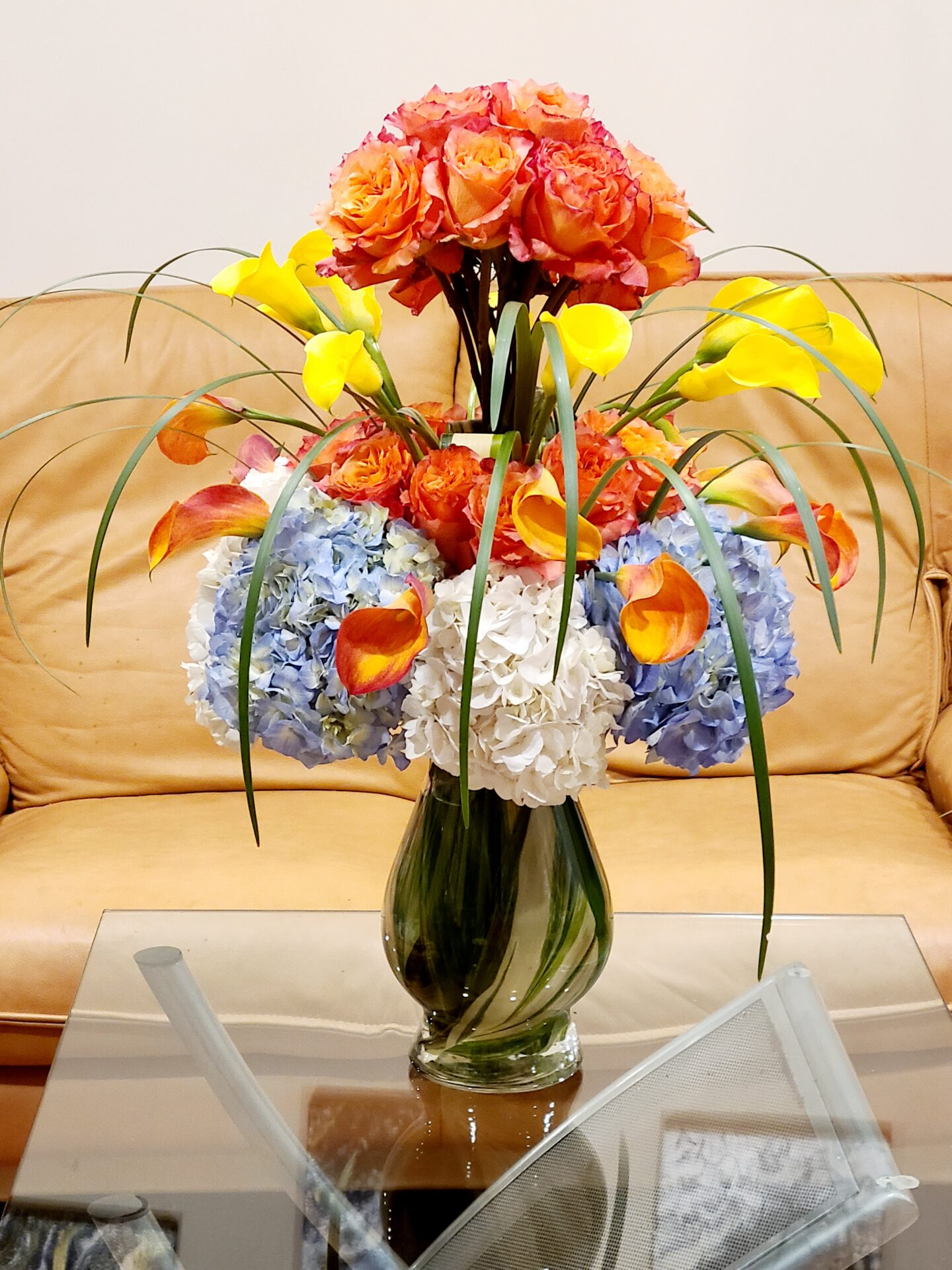A vase of flowers sits on a glass table in front of a couch