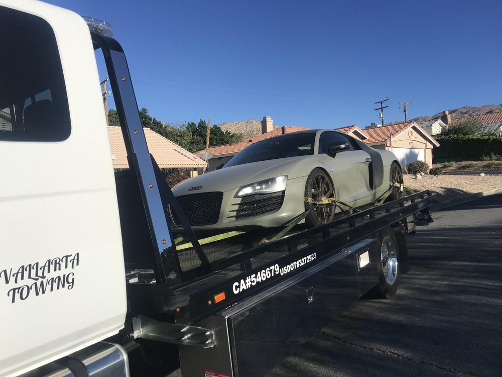 A gray Audi R8 being towed by a white tow truck on a sunny day.