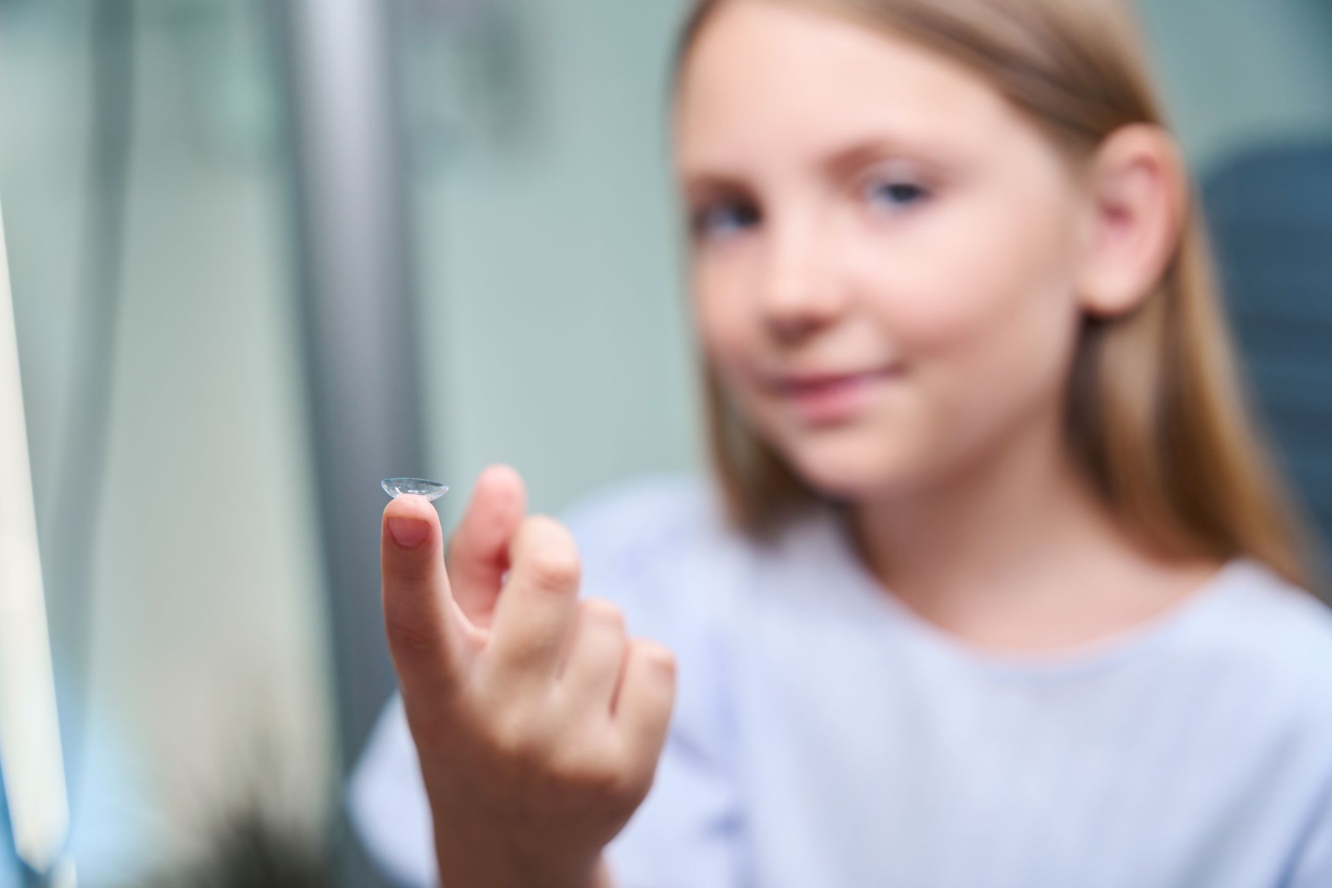 Mädchen hält eine Kontaktlinse ans Auge, verschwommener Innenraumhintergrund