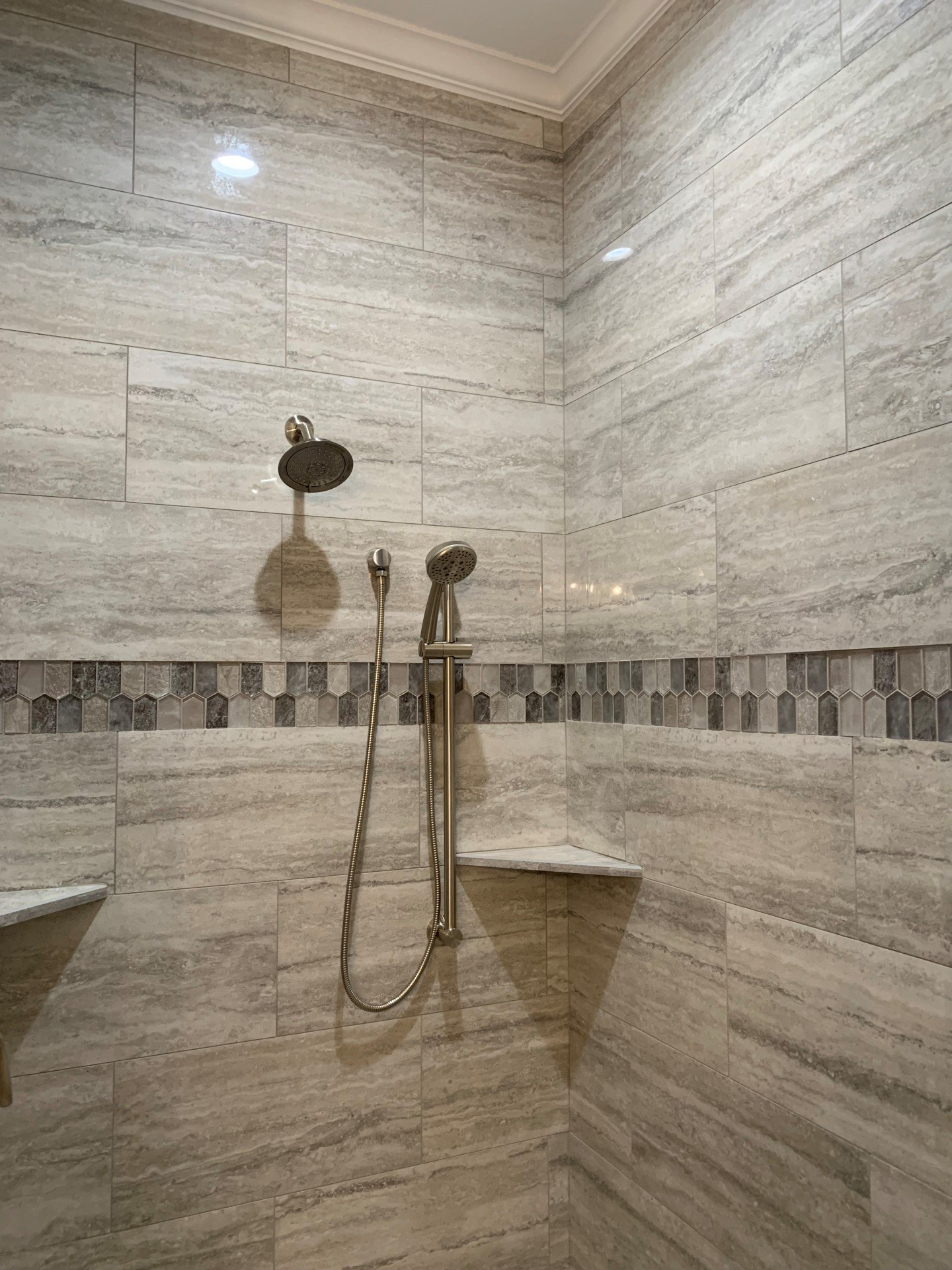 A shower with a shower head and a shelf in a bathroom.