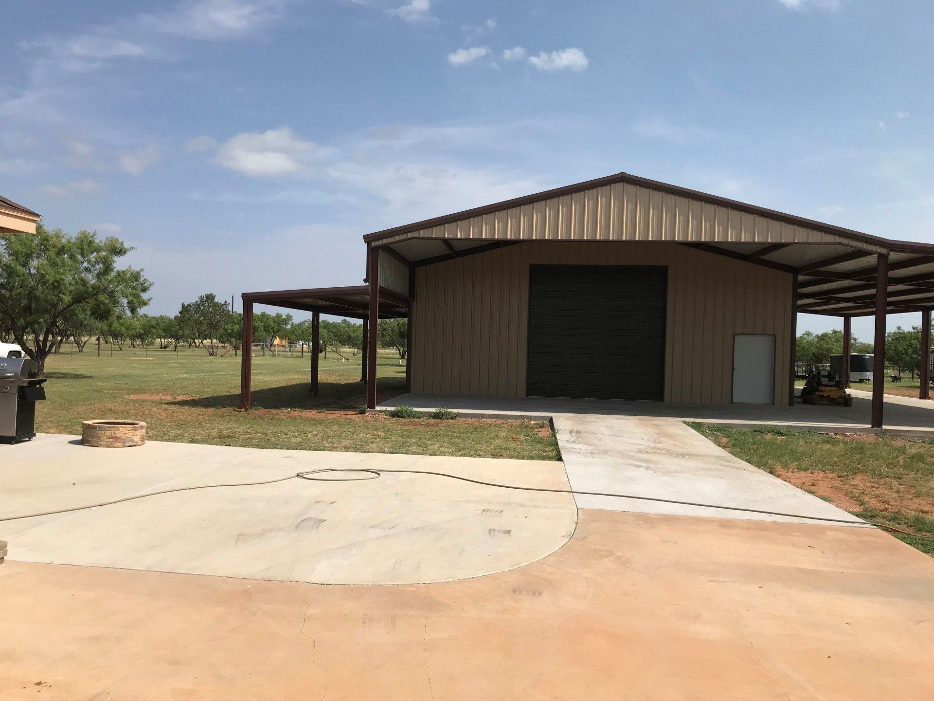A large metal building with a large garage door is sitting in the middle of a field.
