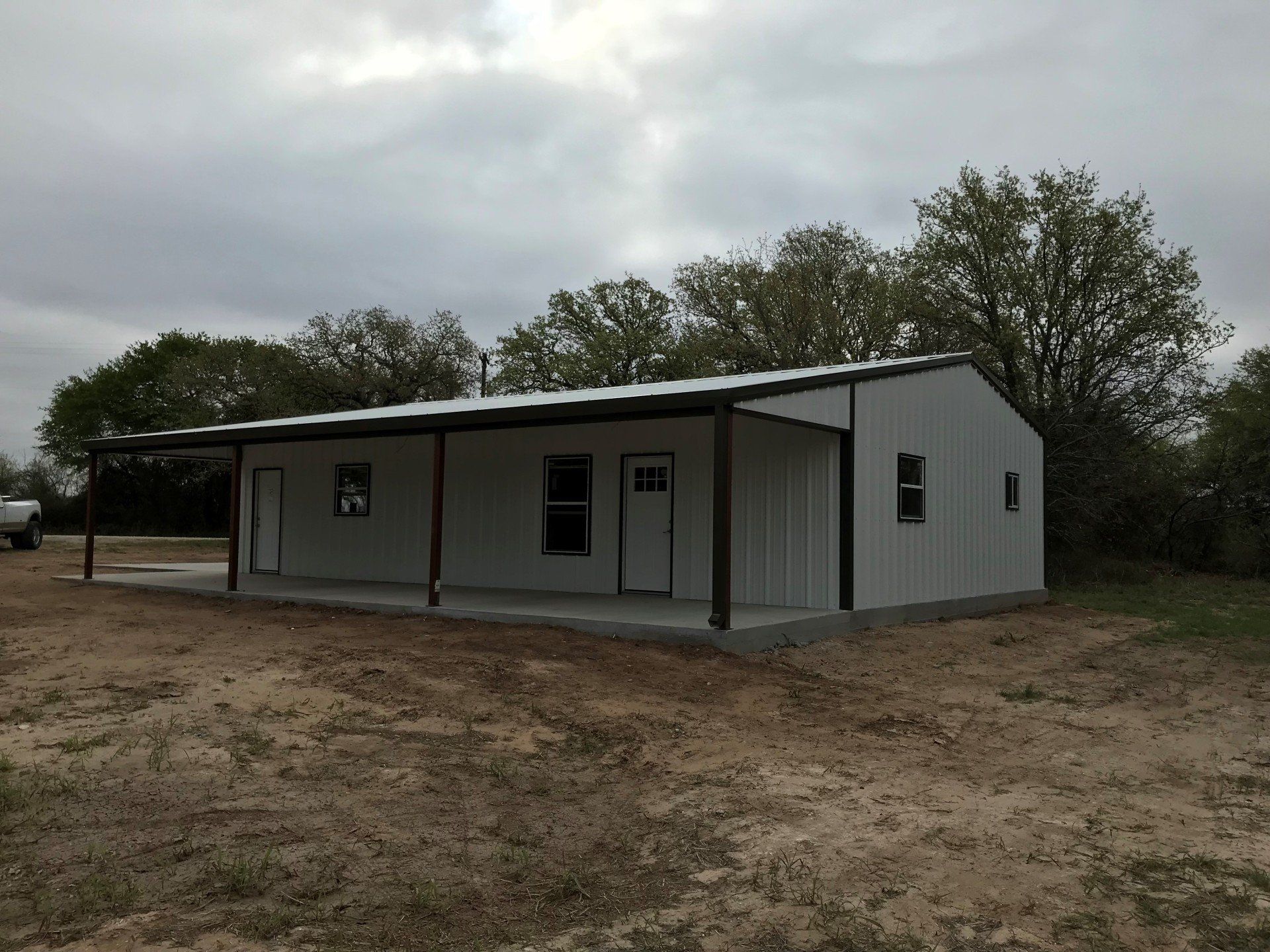 A white house with a porch is sitting in the middle of a dirt field.