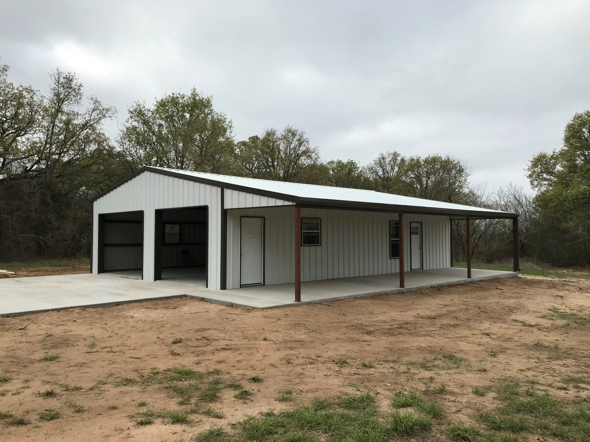 A large white metal building with a porch and trees in the background