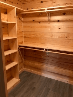 A walk in closet with wooden shelves and a wooden floor.