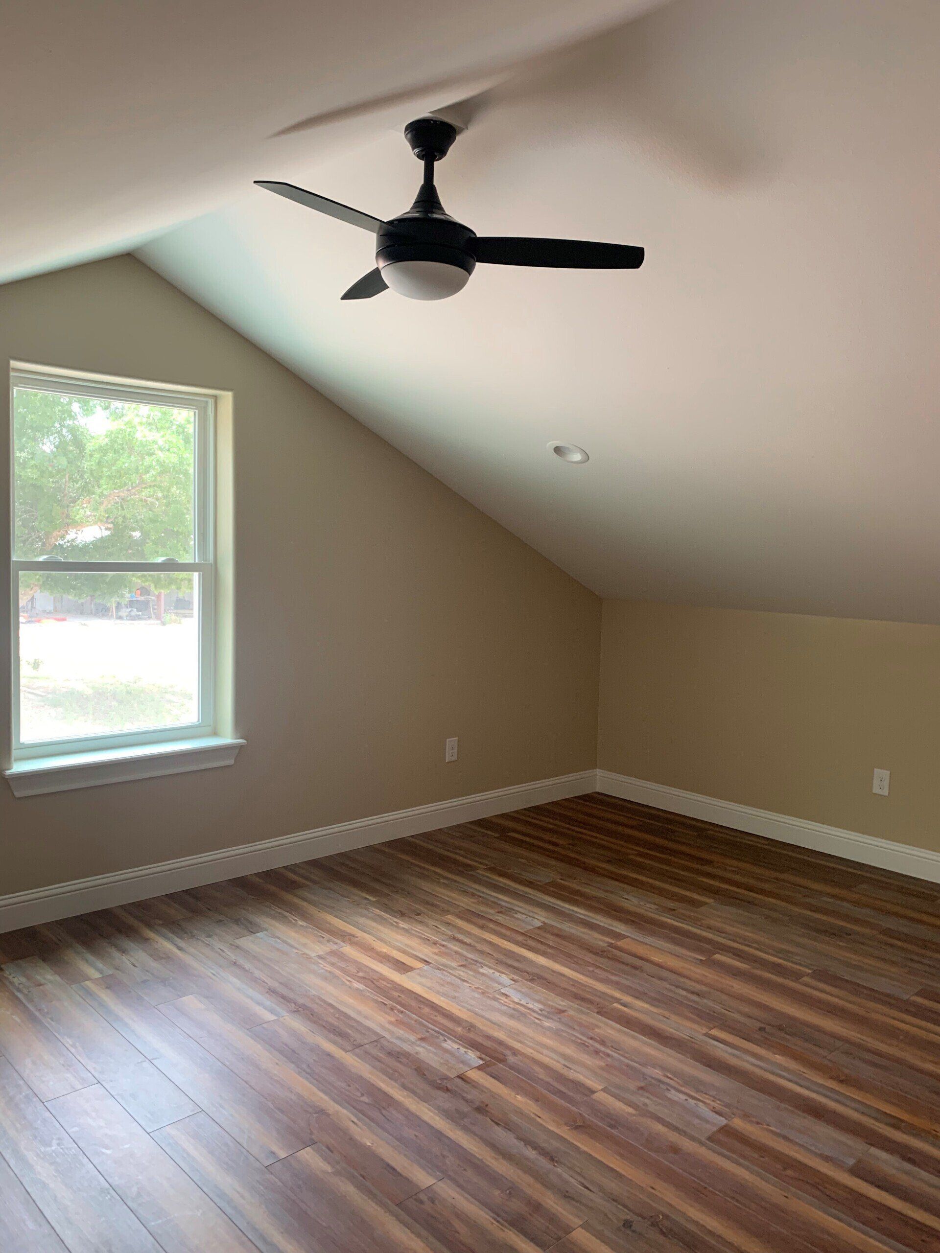 An empty room with a ceiling fan and a window.