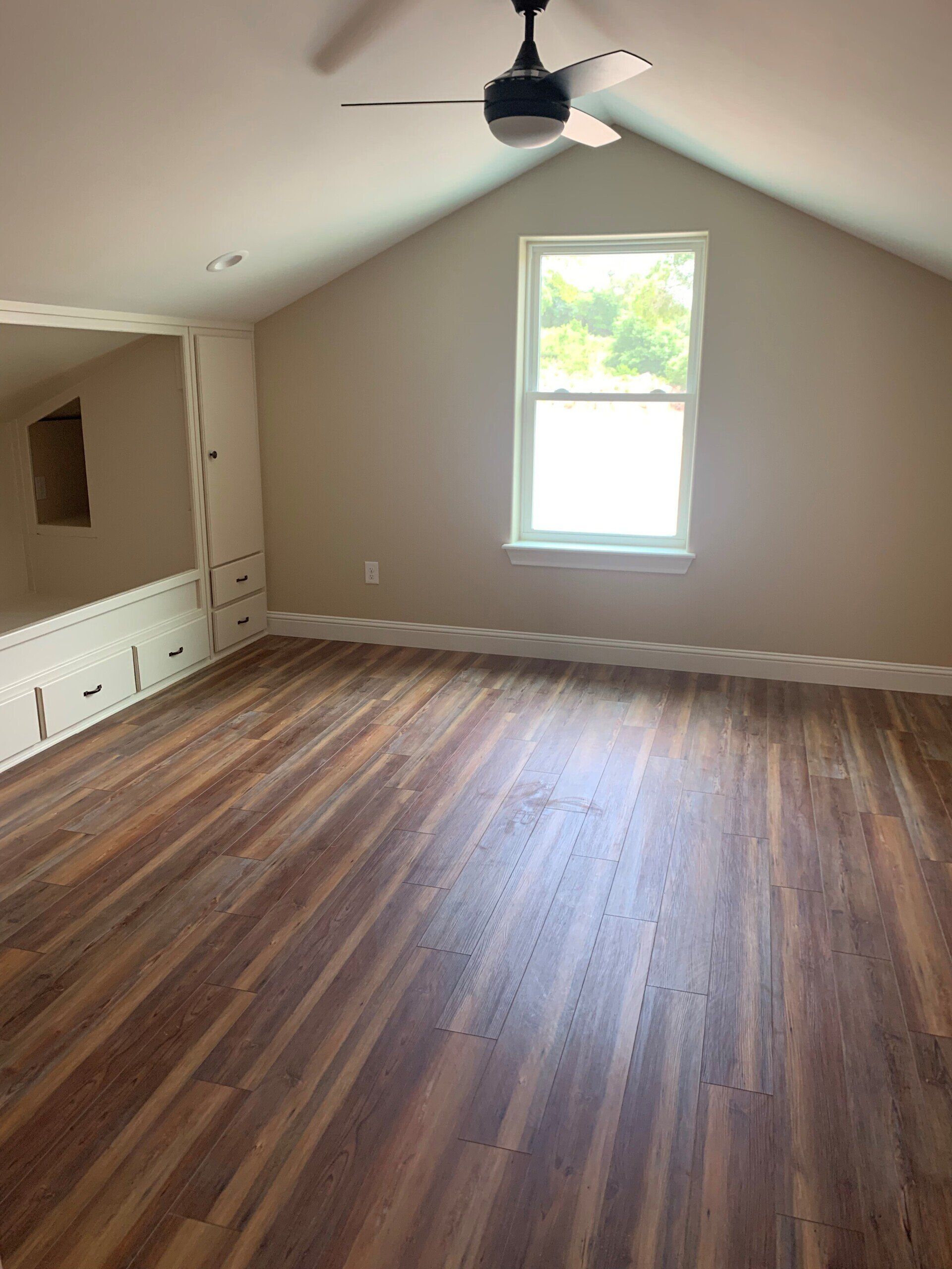 An empty room with a ceiling fan and a window.