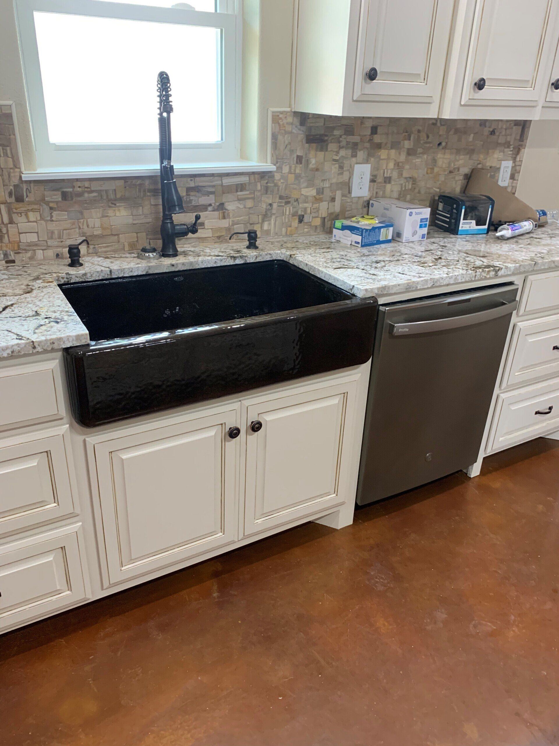 A kitchen with a black sink , white cabinets , and a stainless steel dishwasher.