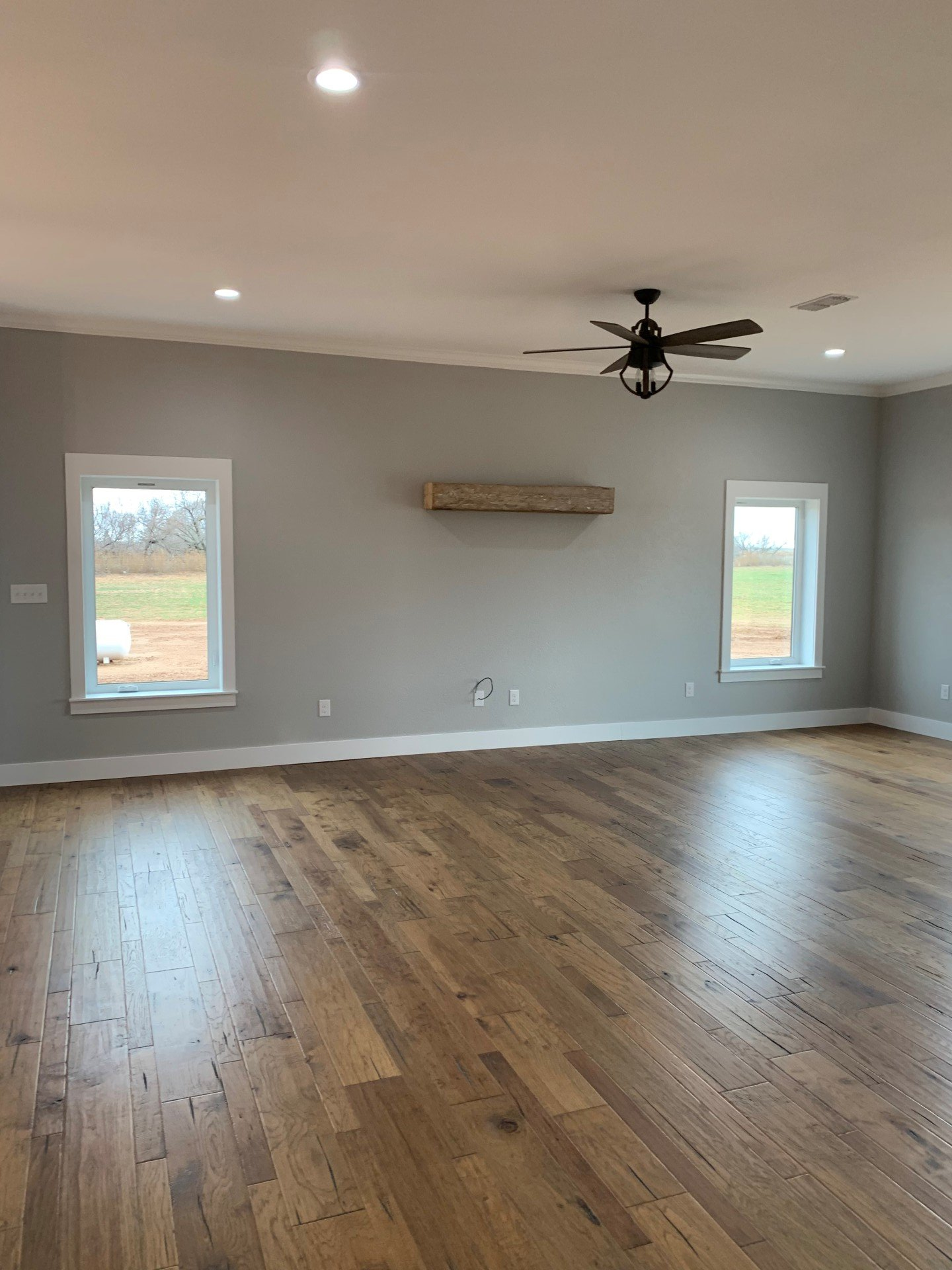 An empty living room with hardwood floors and a ceiling fan.