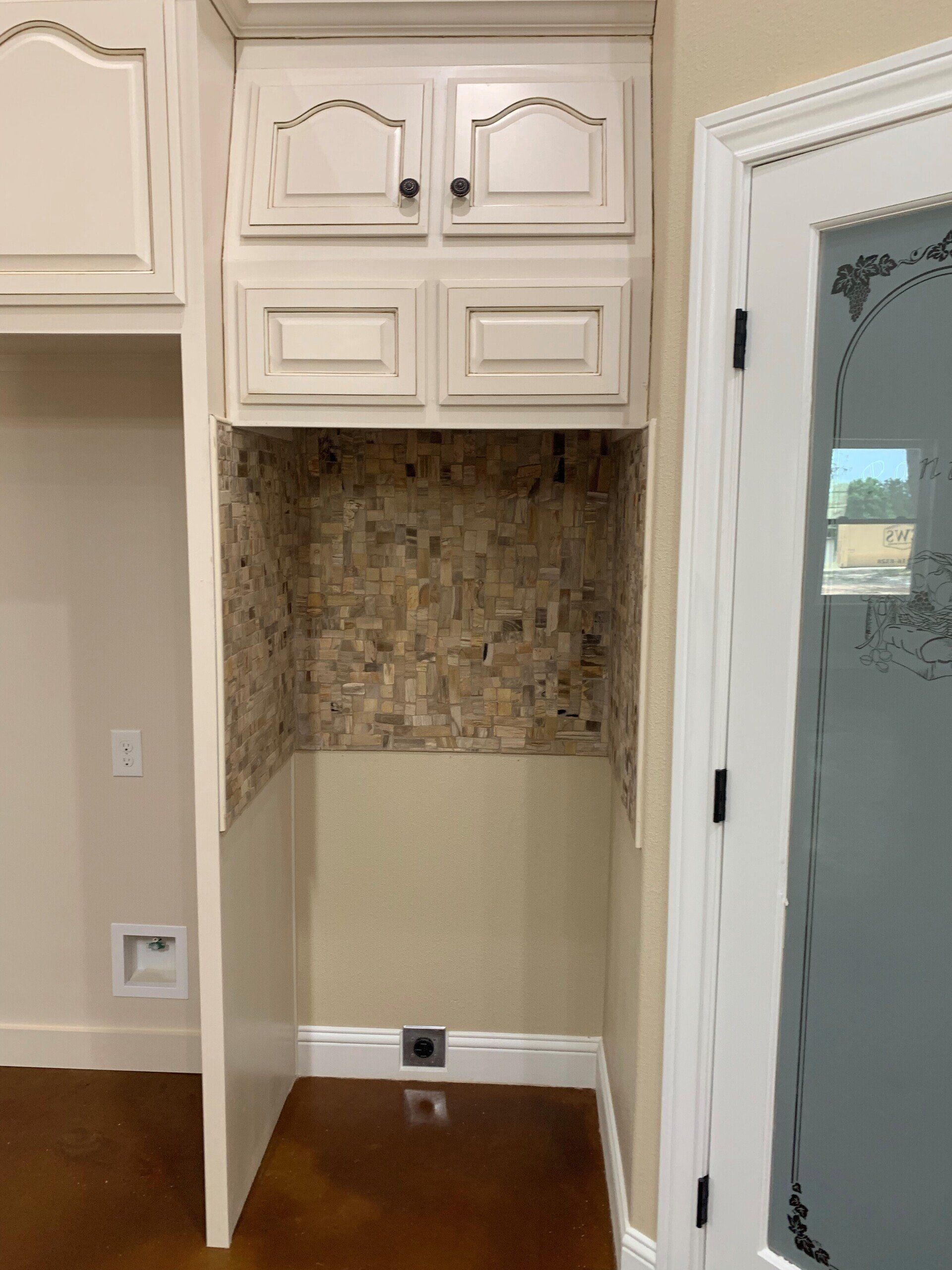 A laundry room with white cabinets and a glass door.