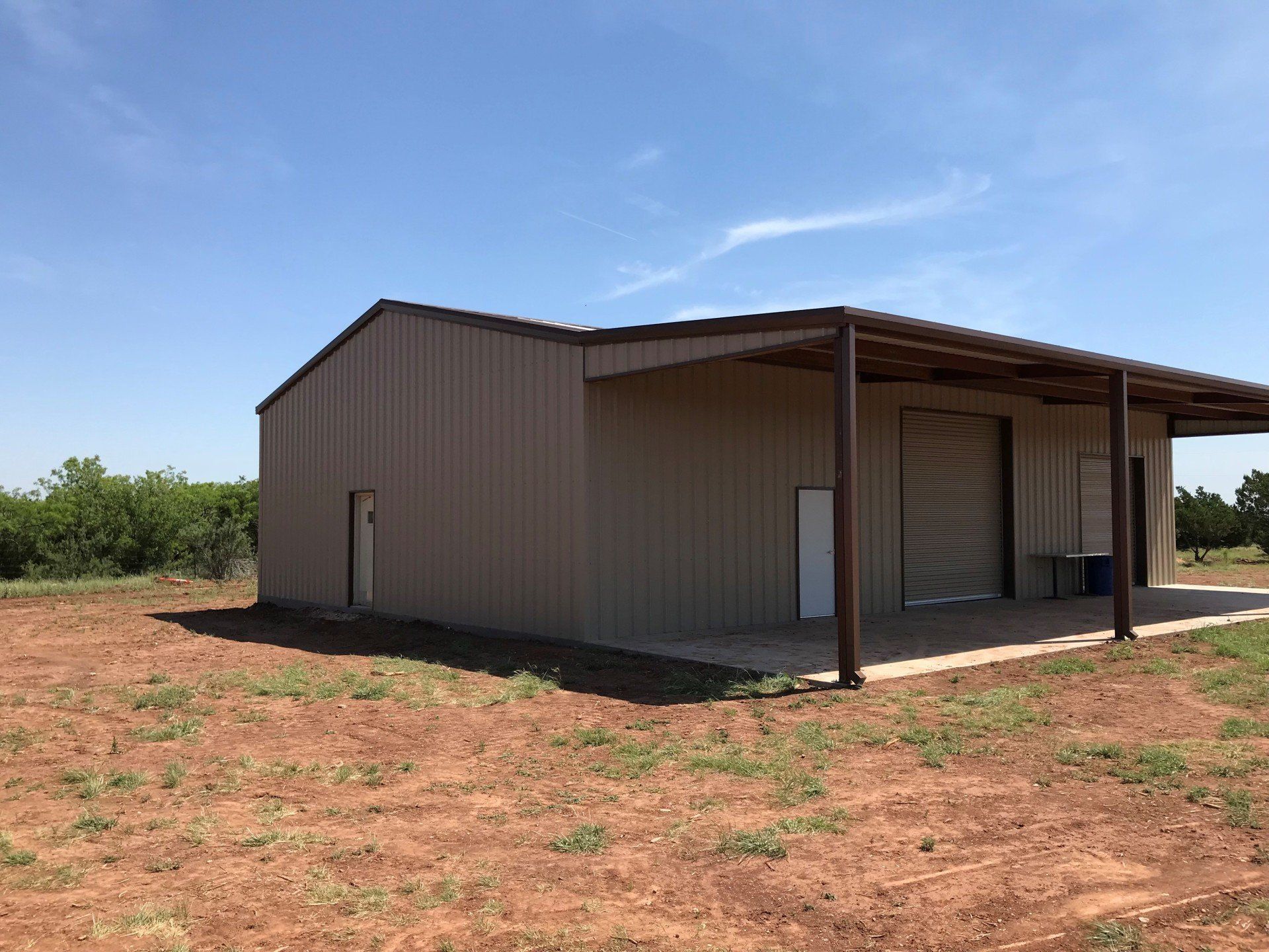A large metal building with a covered porch is sitting in the middle of a dirt field.
