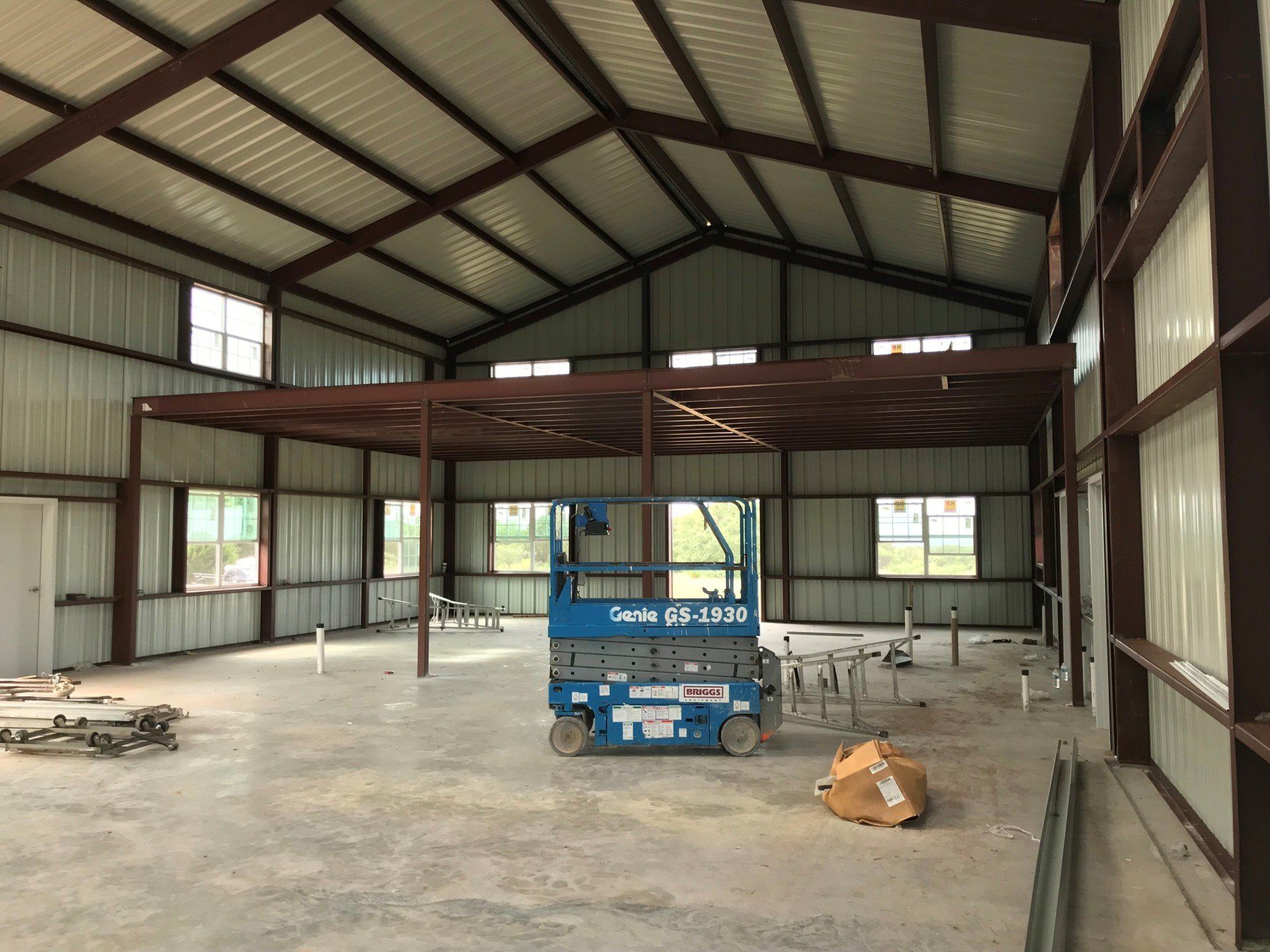 A blue scissor lift is sitting inside of a large metal building.