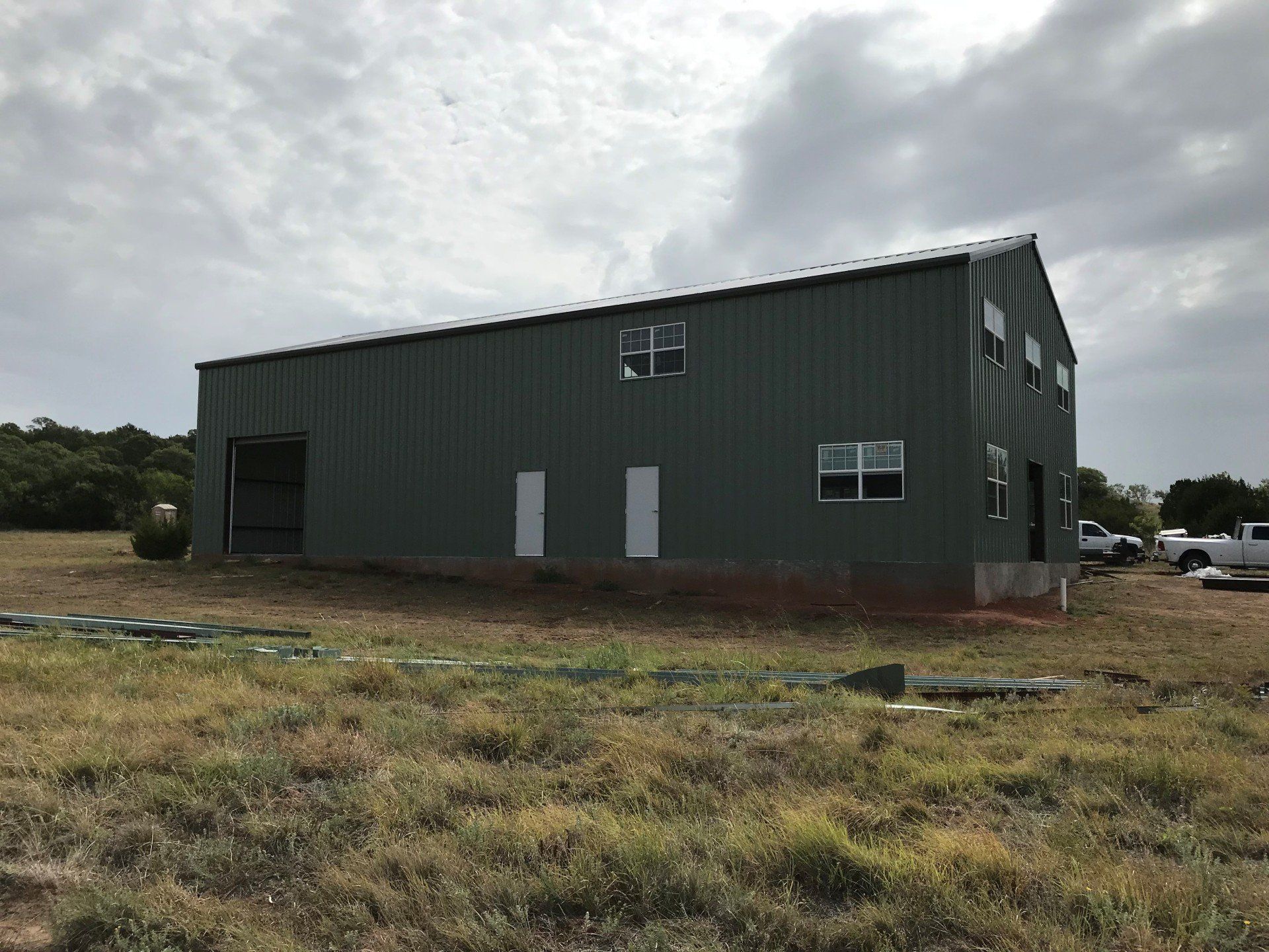 A green building with white windows is sitting in the middle of a grassy field.