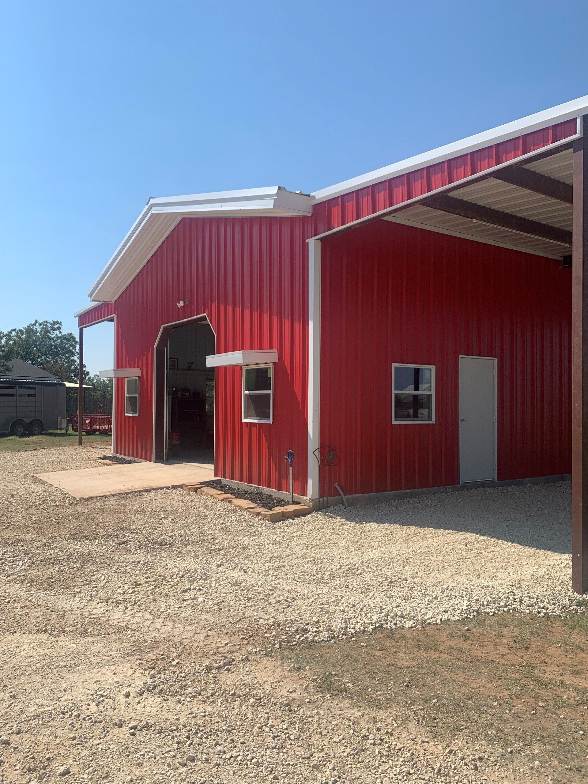A large red barn with a white roof is sitting on top of a gravel lot.