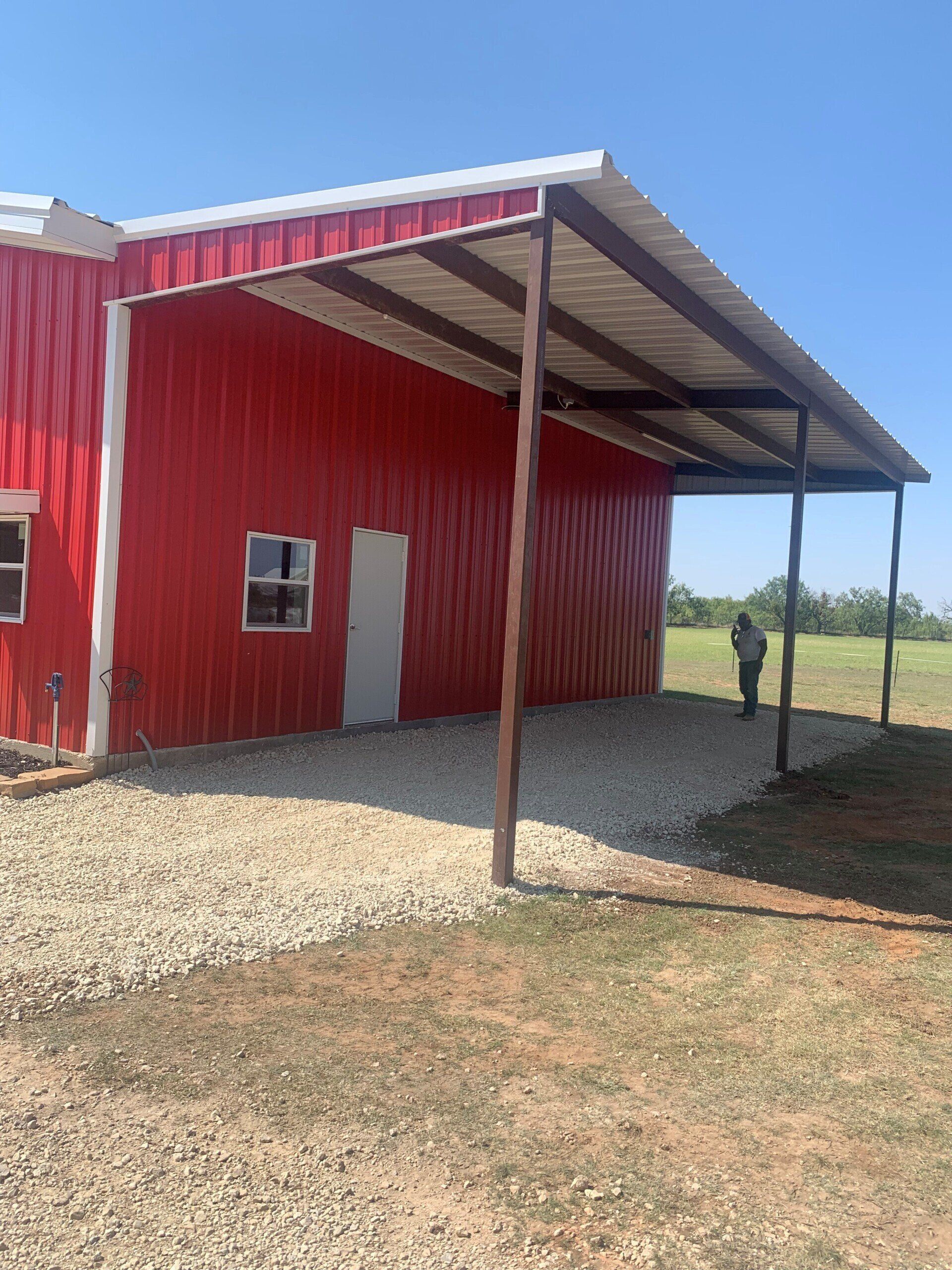 A red barn with a covered area in front of it.