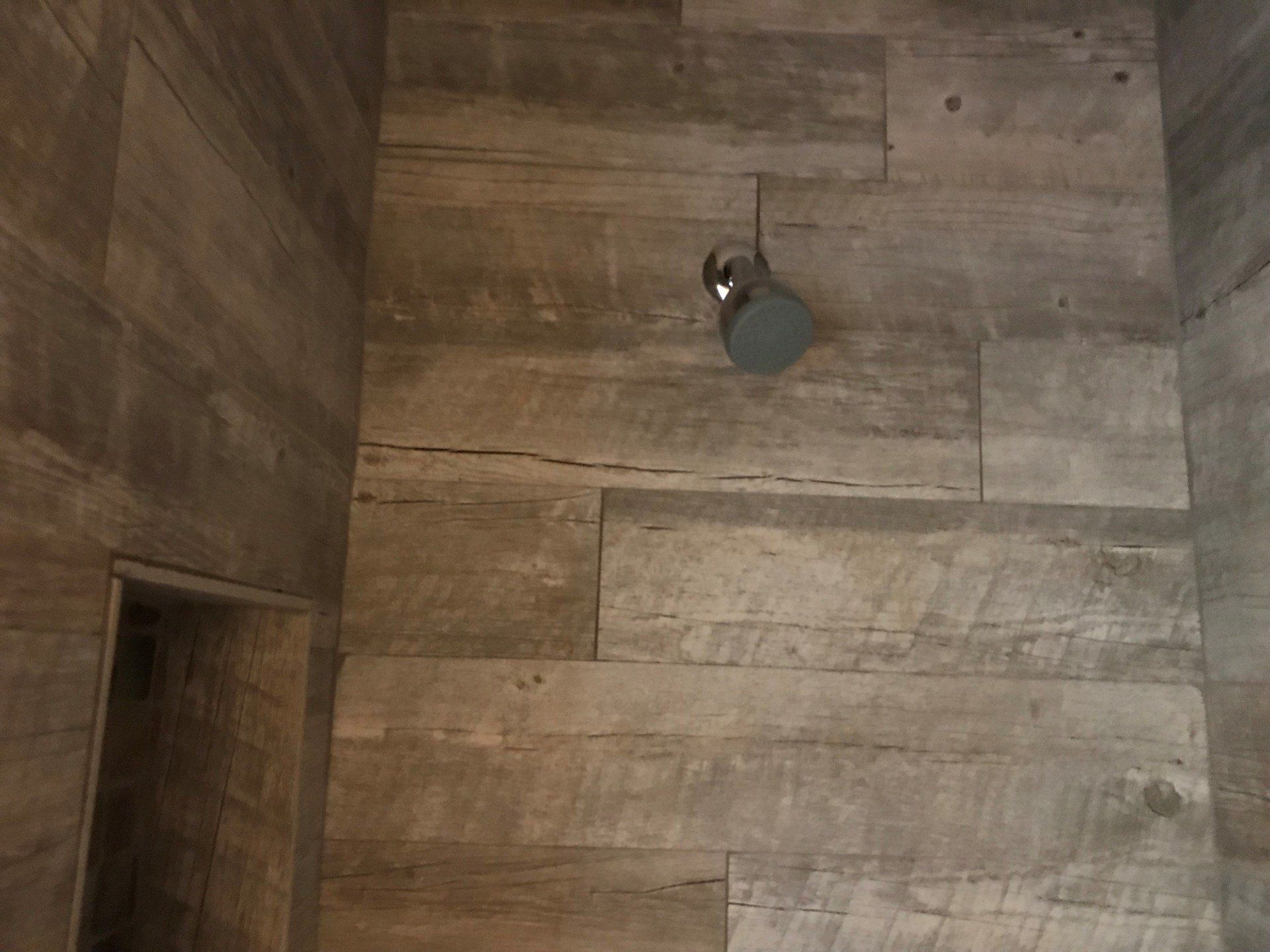 A shower head is hanging from the ceiling of a bathroom with wooden tiles.