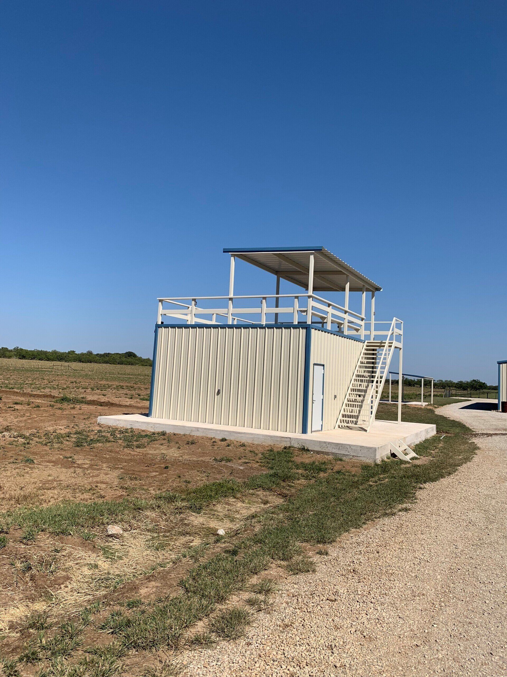 A building with stairs leading up to it is in the middle of a field.