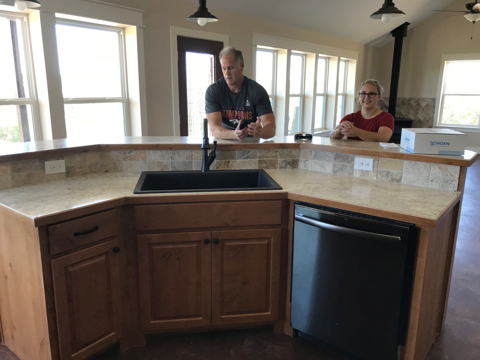 A man and a woman are standing in a kitchen looking at a sink.