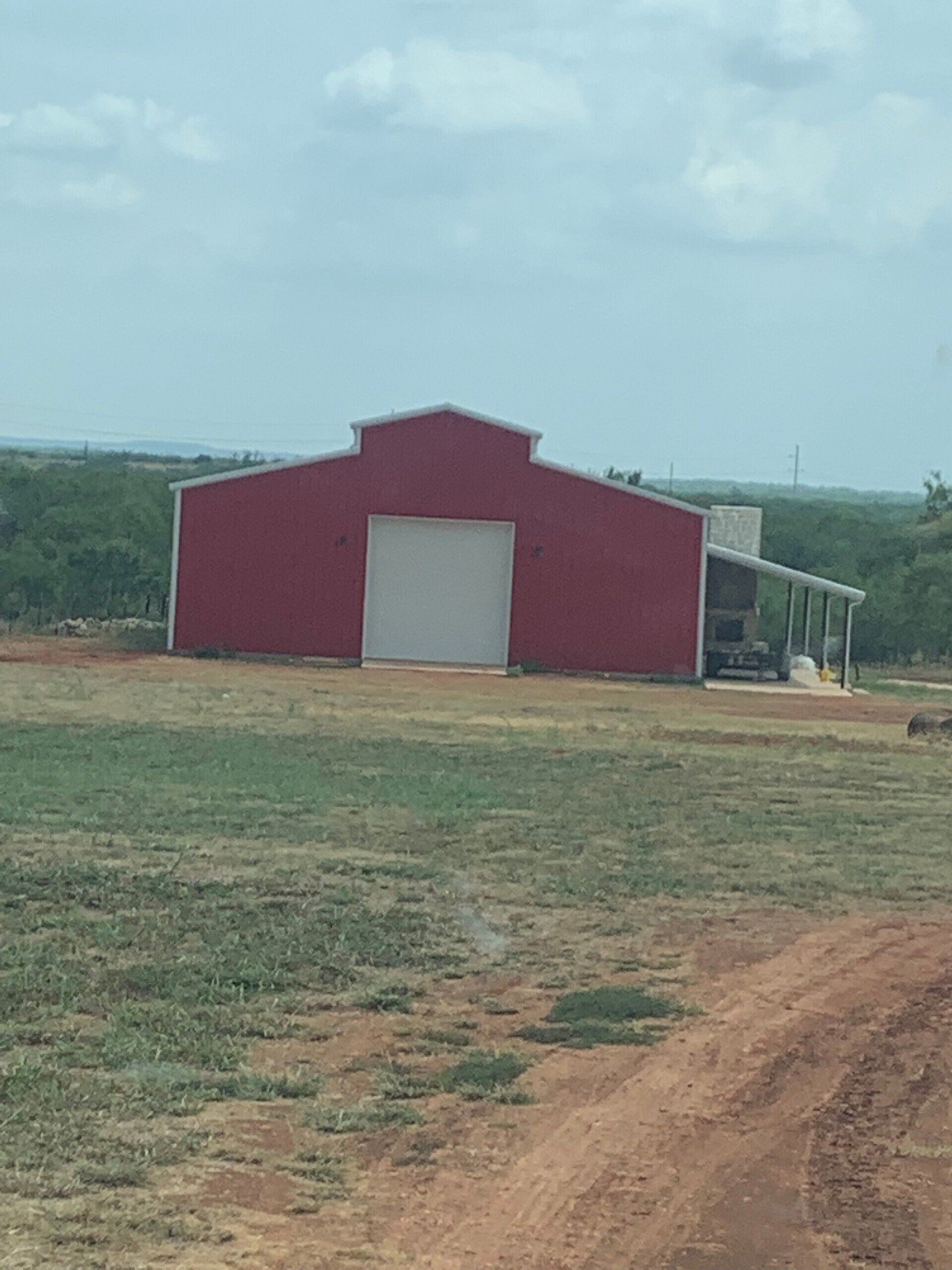 A red barn with a white door is in the middle of a field.