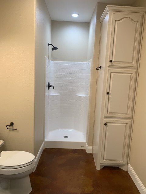 A bathroom with a toilet , shower and cabinets.
