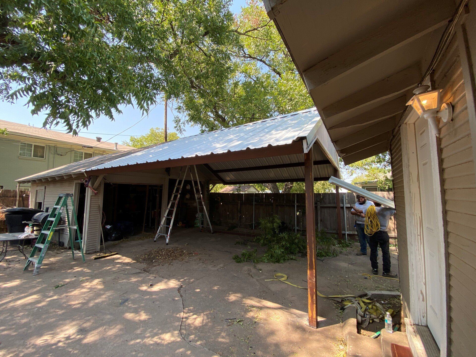 A man is working on a metal roof in the backyard of a house.