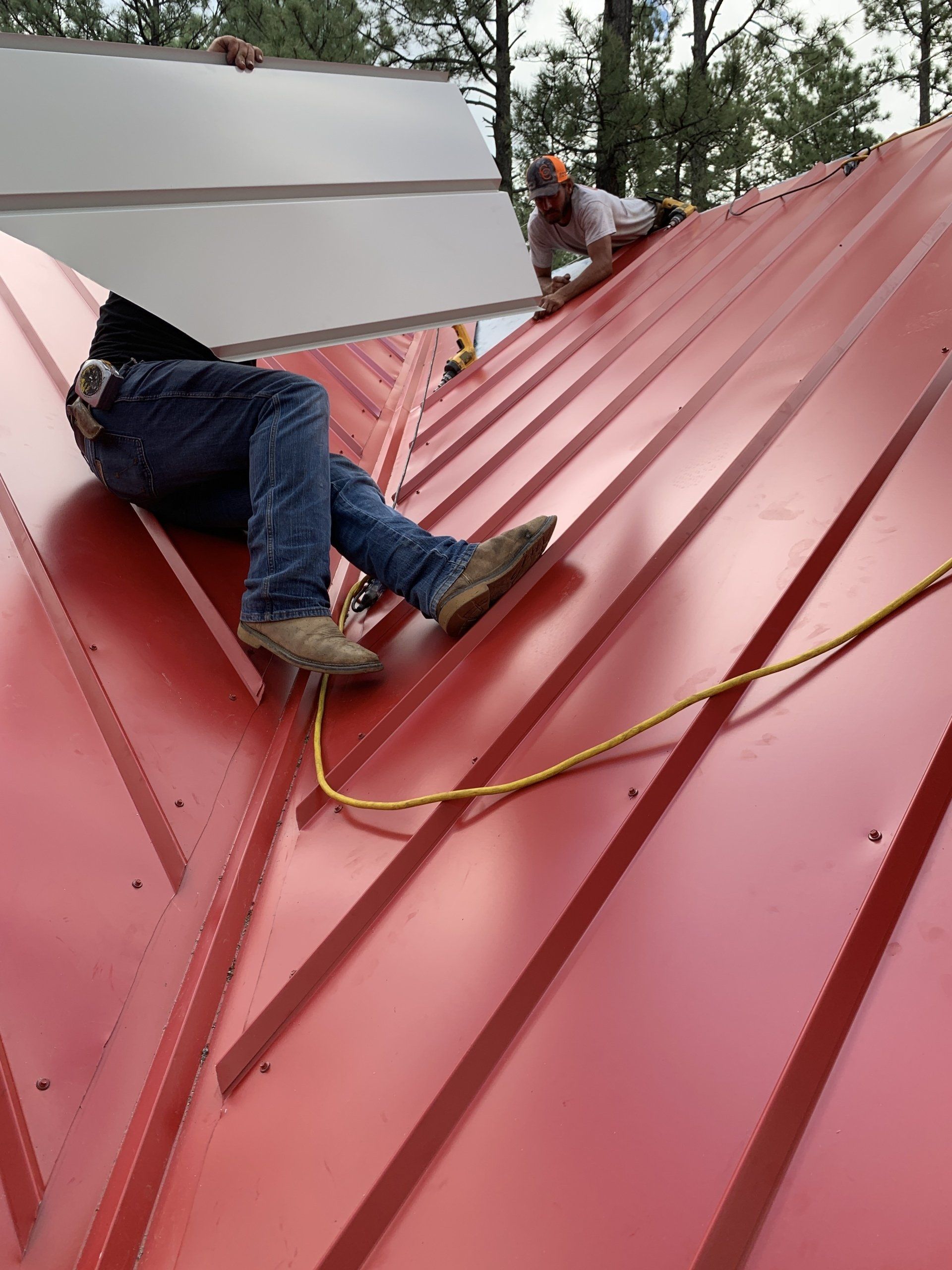 Two men are working on a red metal roof.