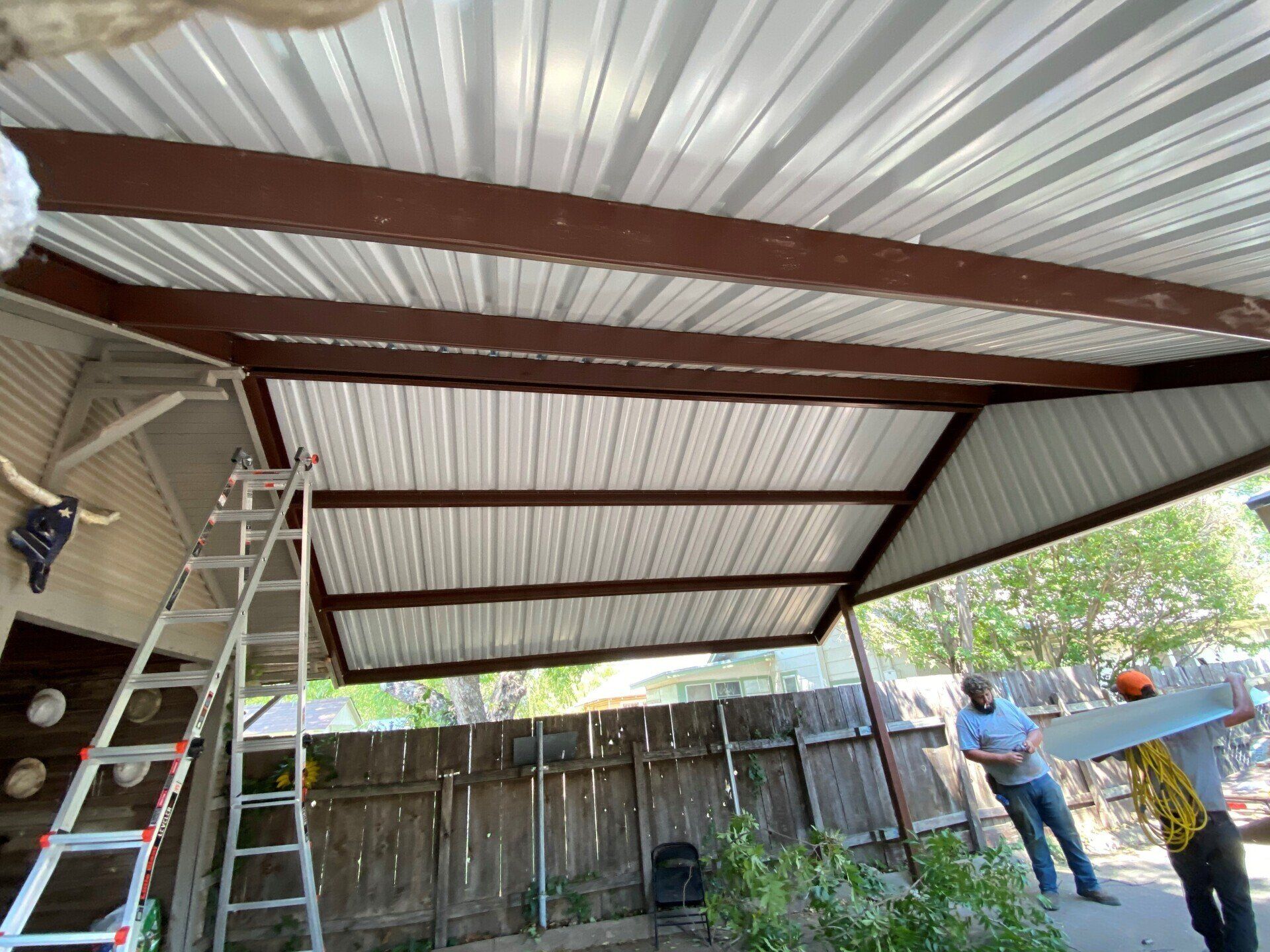 A man is standing under a metal roof with a ladder.