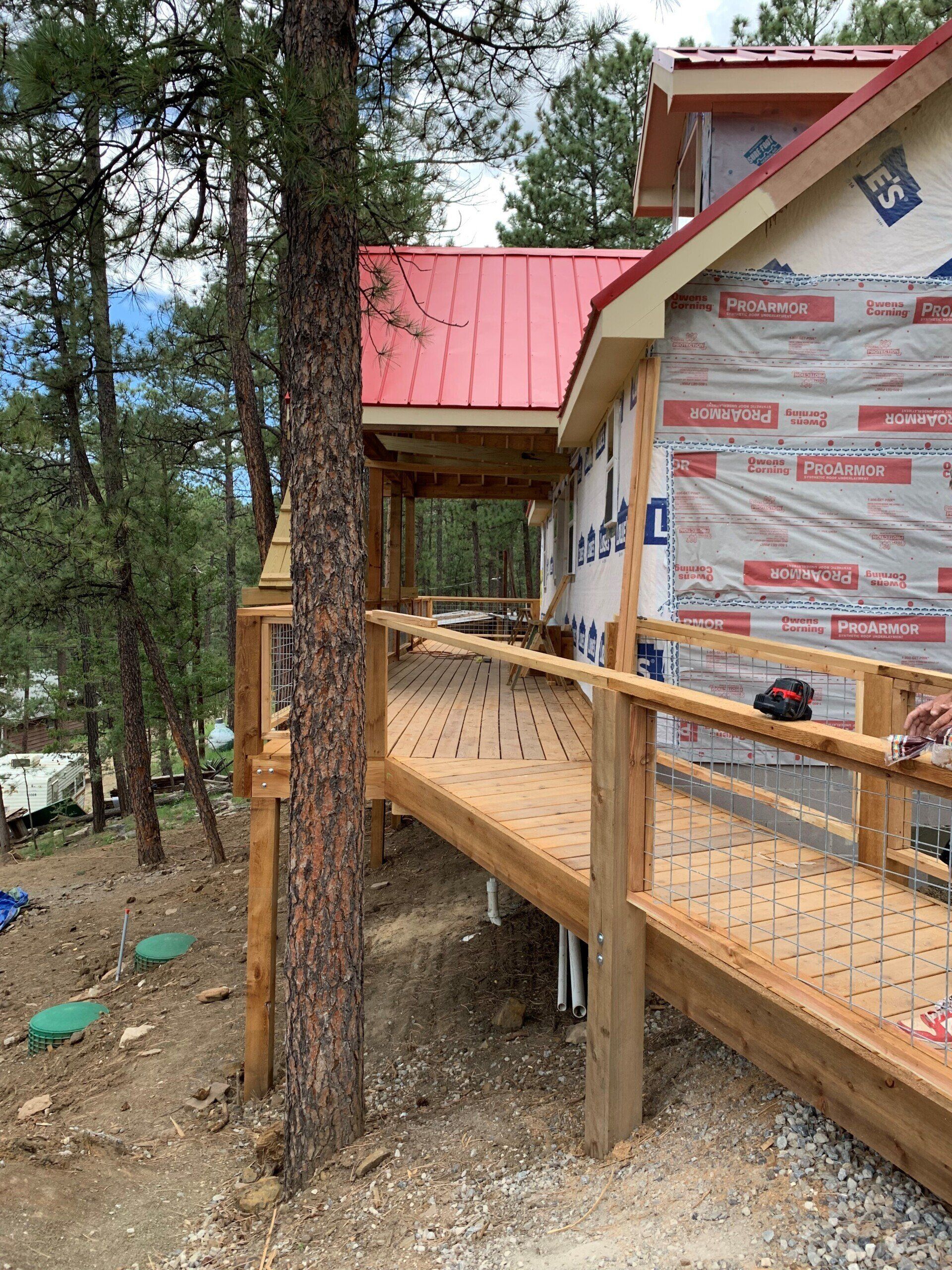 A wooden deck is being built on the side of a house with a red roof.