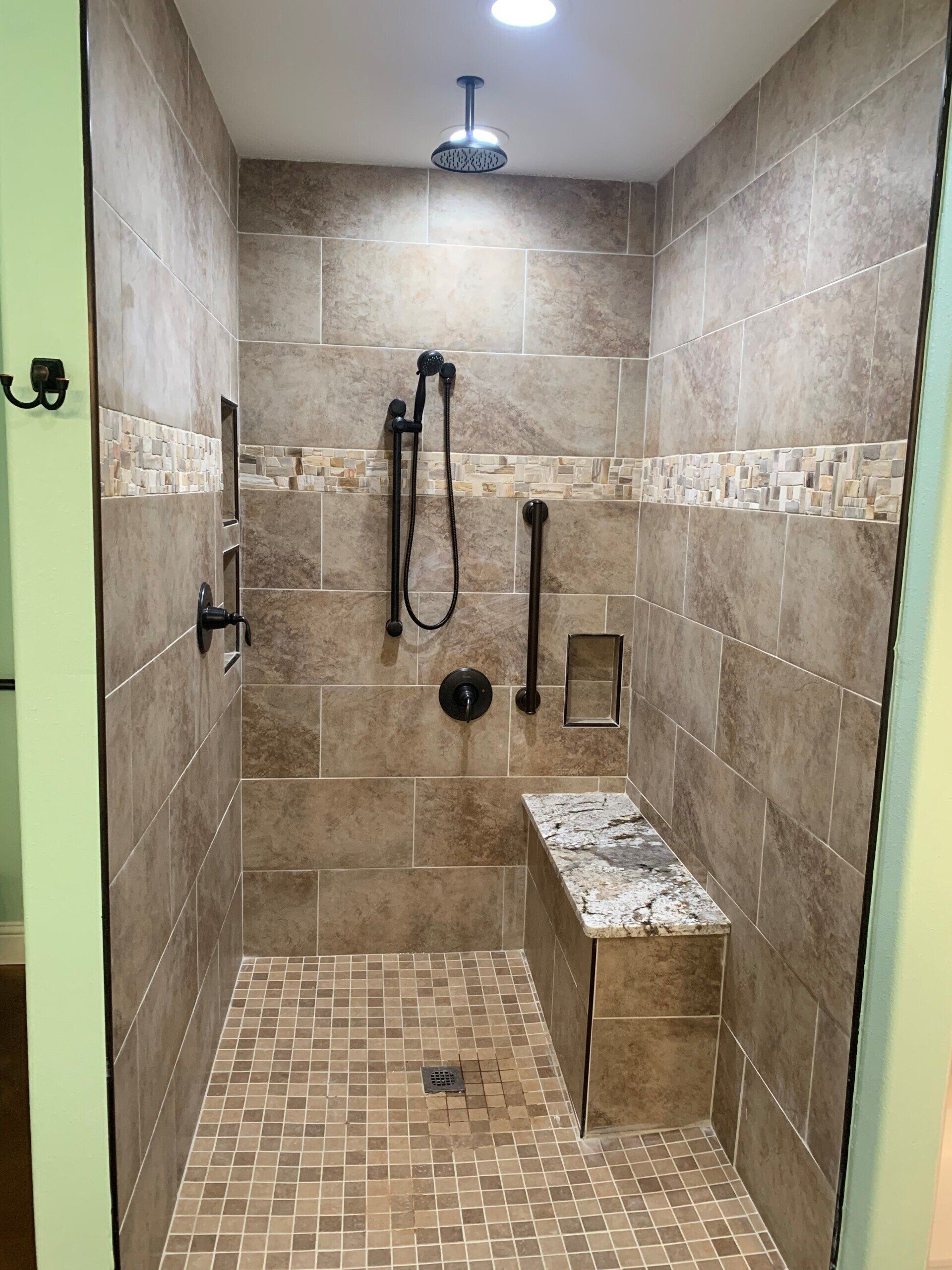 A walk in shower with a bench and a shower head.