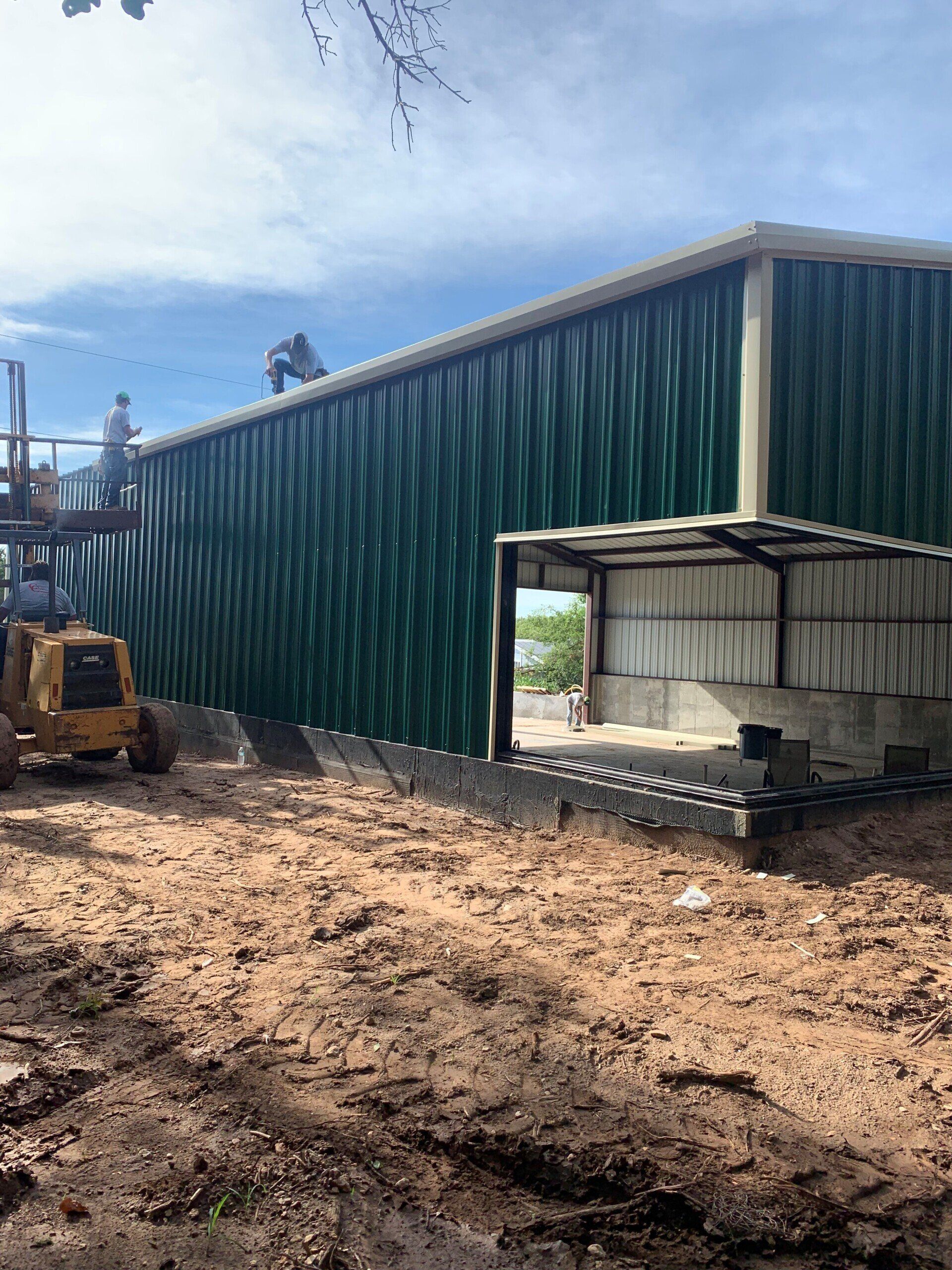 A large green building is being built on a dirt field.
