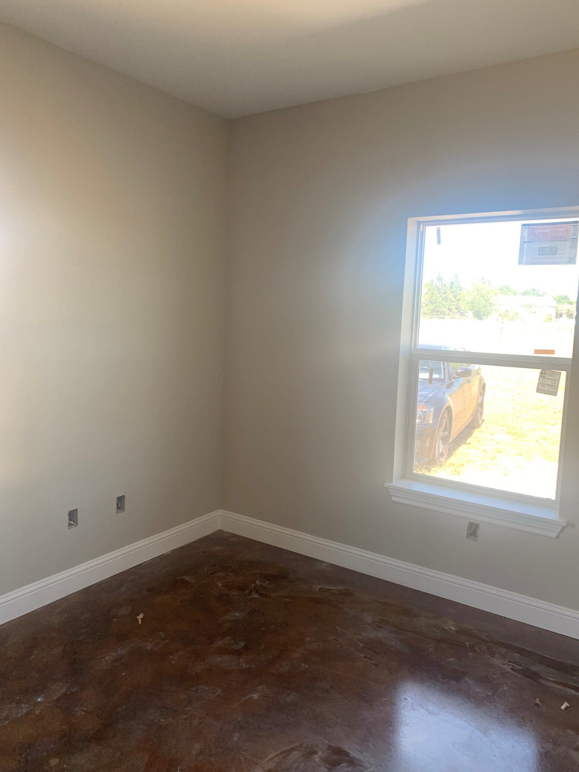 An empty room with a window and a wooden floor.
