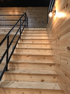 A wooden staircase with a metal railing and a light on the wall.