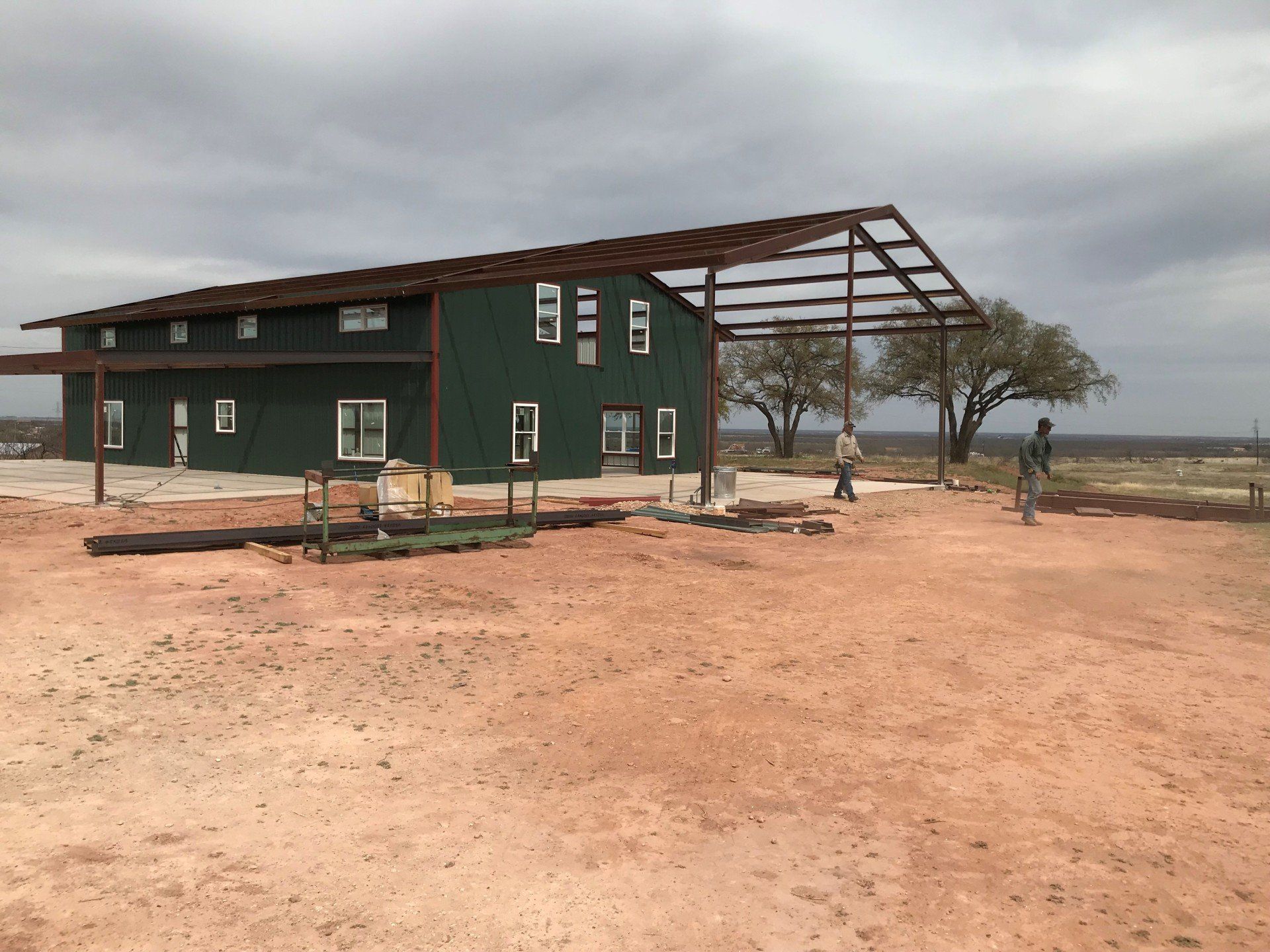 A green building is being built in the middle of a dirt field.