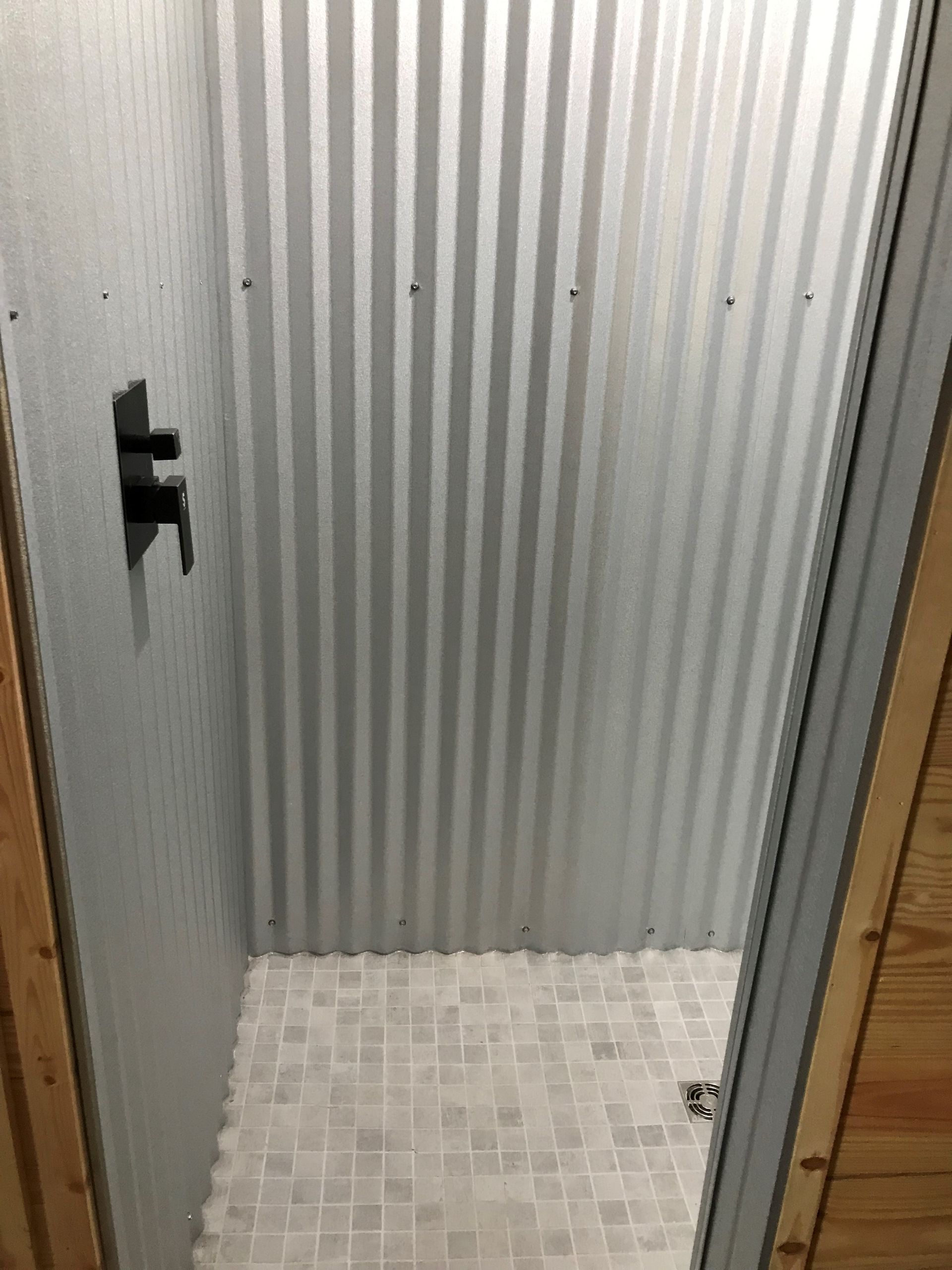A shower with a metal wall and a tiled floor.