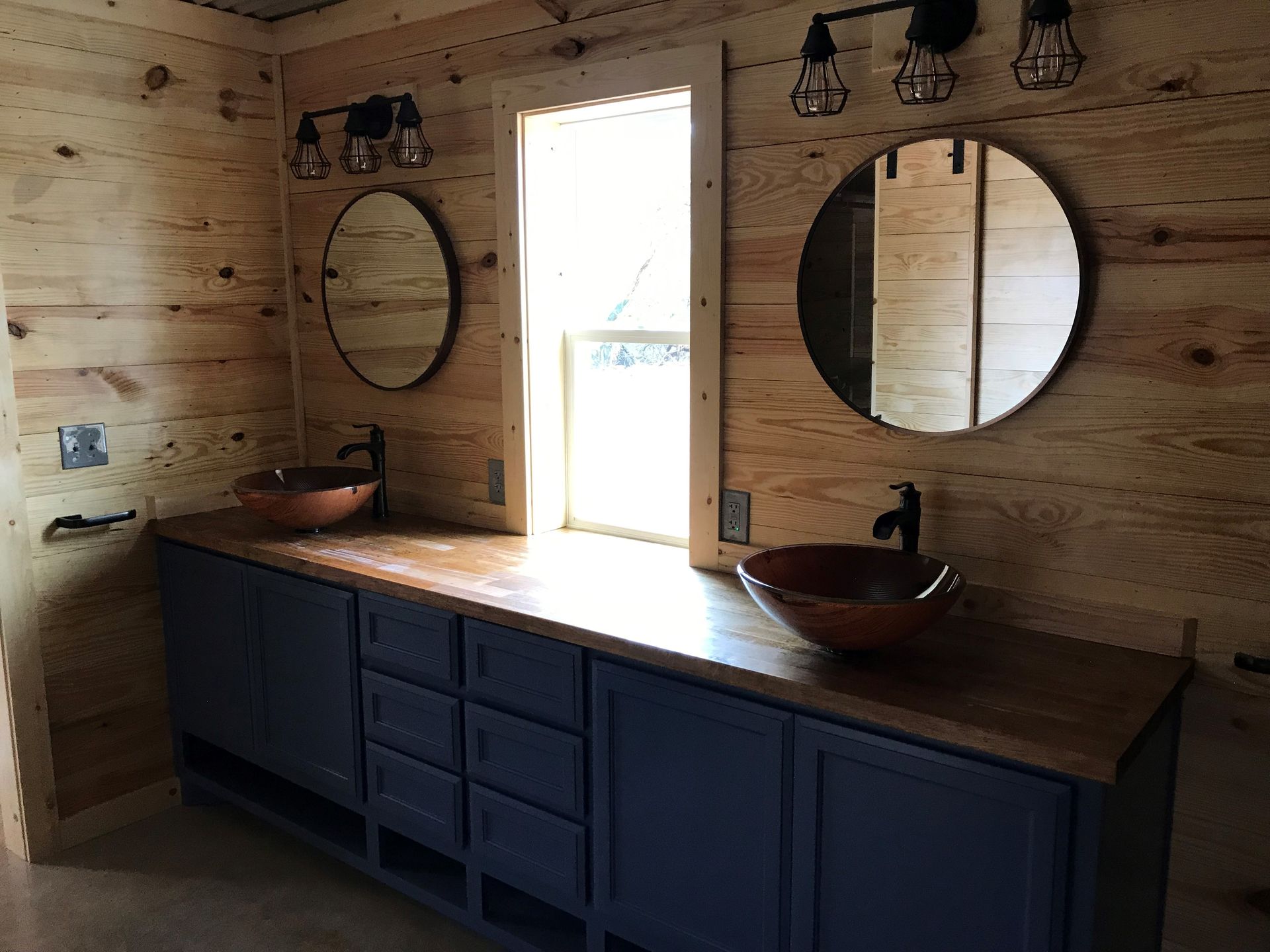 A bathroom with two sinks , two mirrors and a window.