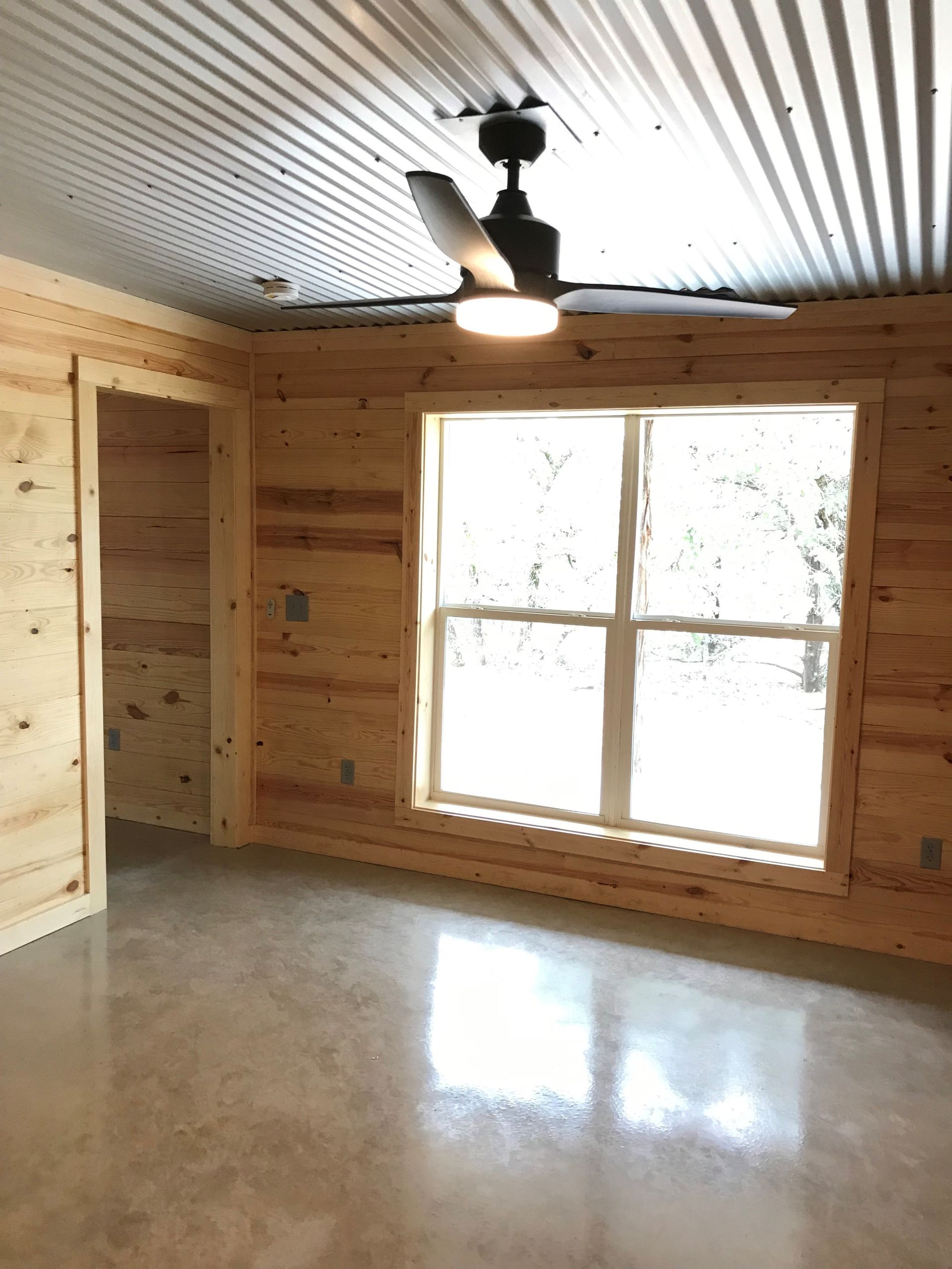 An empty room with a ceiling fan and a window.