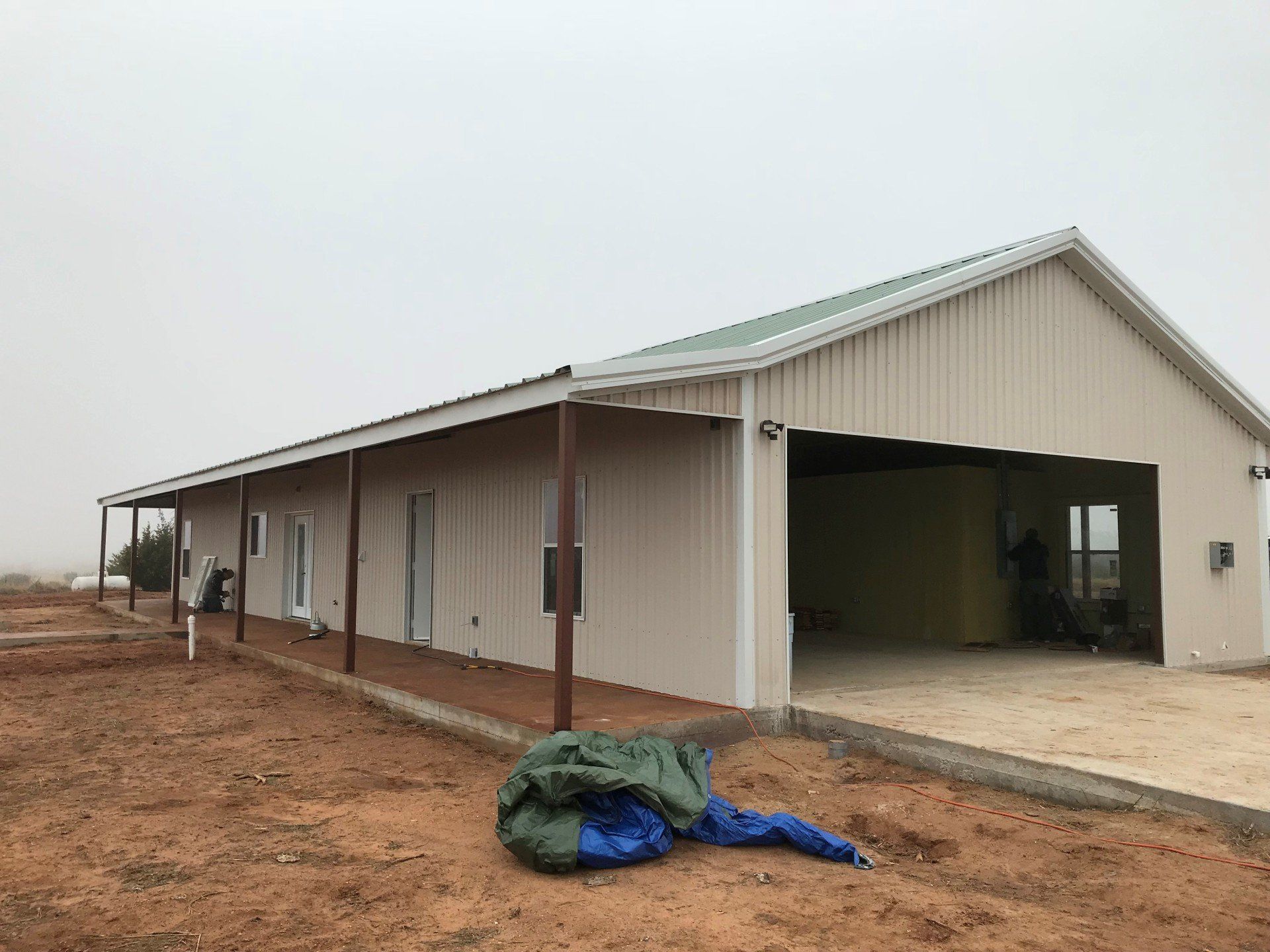 A large white building with a green roof is sitting in the middle of a dirt field.